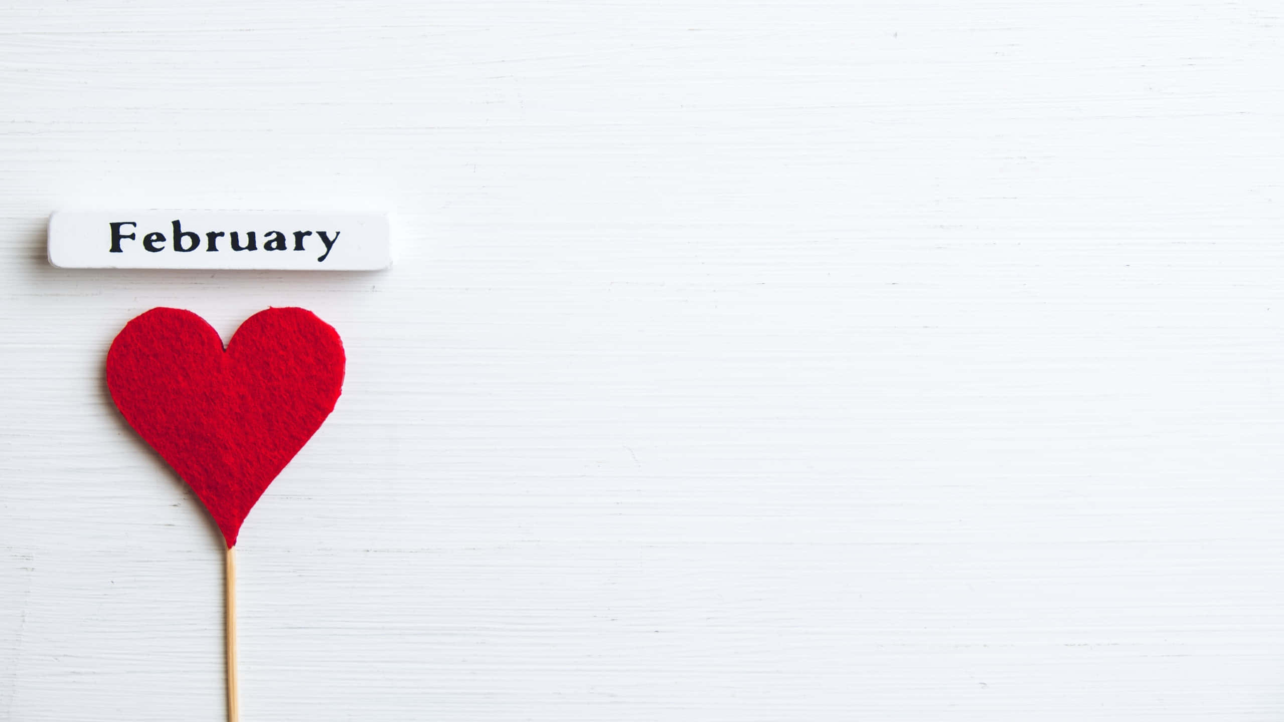 red felt heart, white label reading February, textured white wooden surface, 2K Desktop Wallpaper