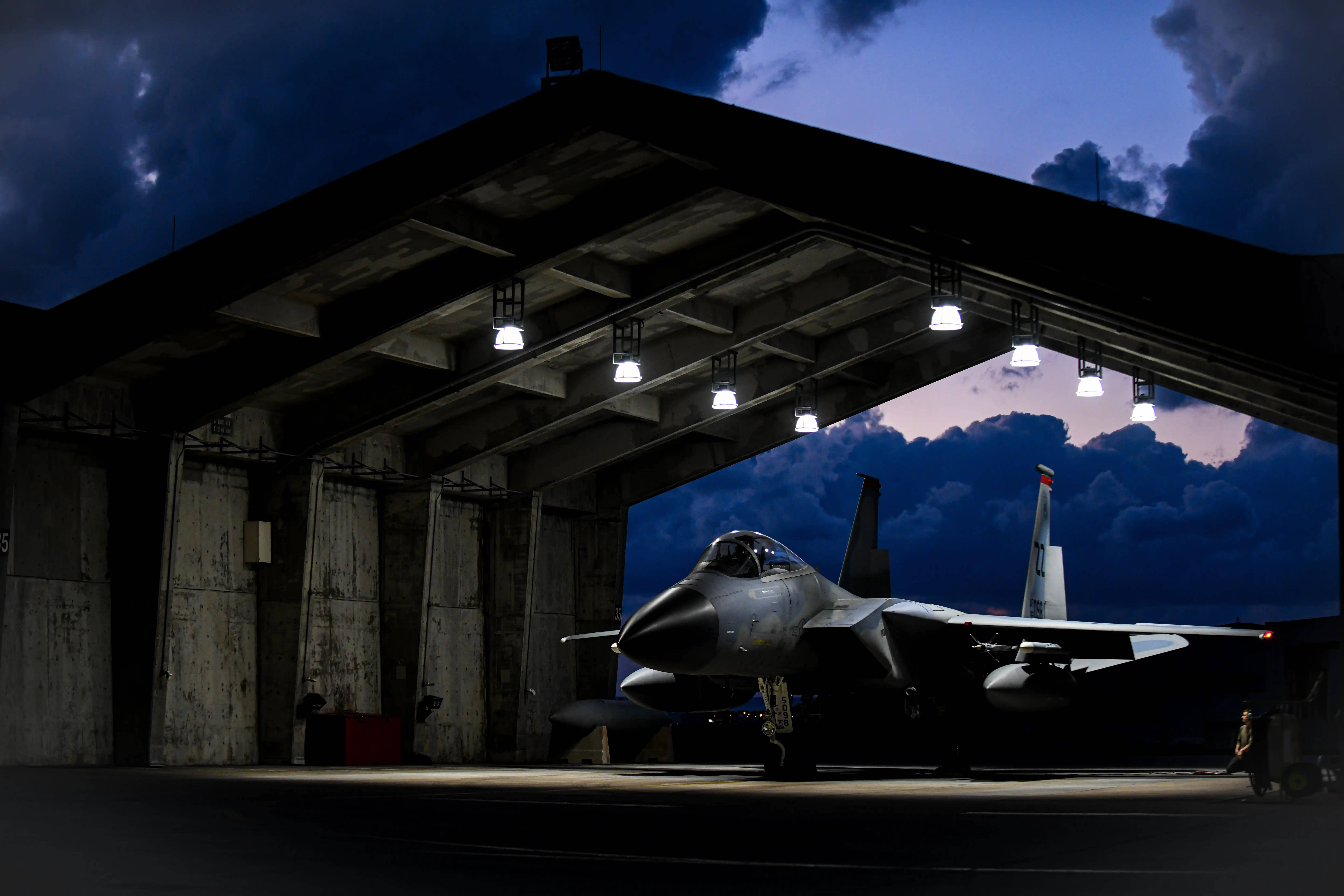 F-15 Fighter Jet, dimly lit hangar, dramatic twilight clouds, 8K Desktop Wallpaper