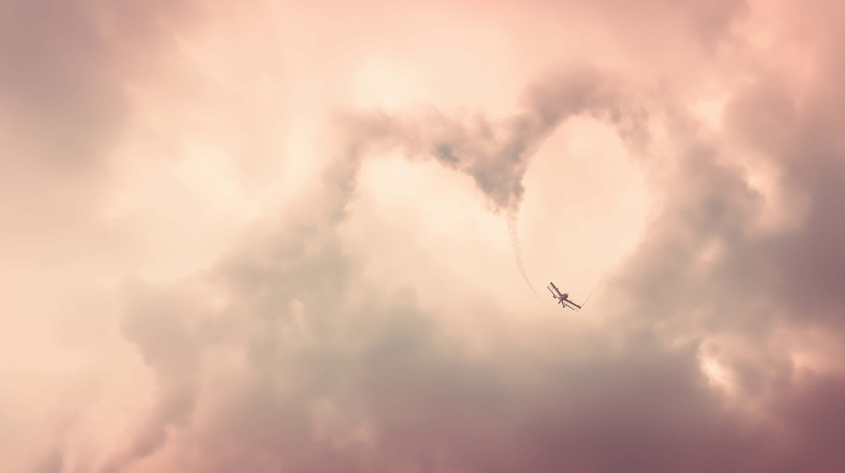 biplane, heart-shaped skywriting, soft pink and peach cloudy sky, 2K Desktop Wallpaper