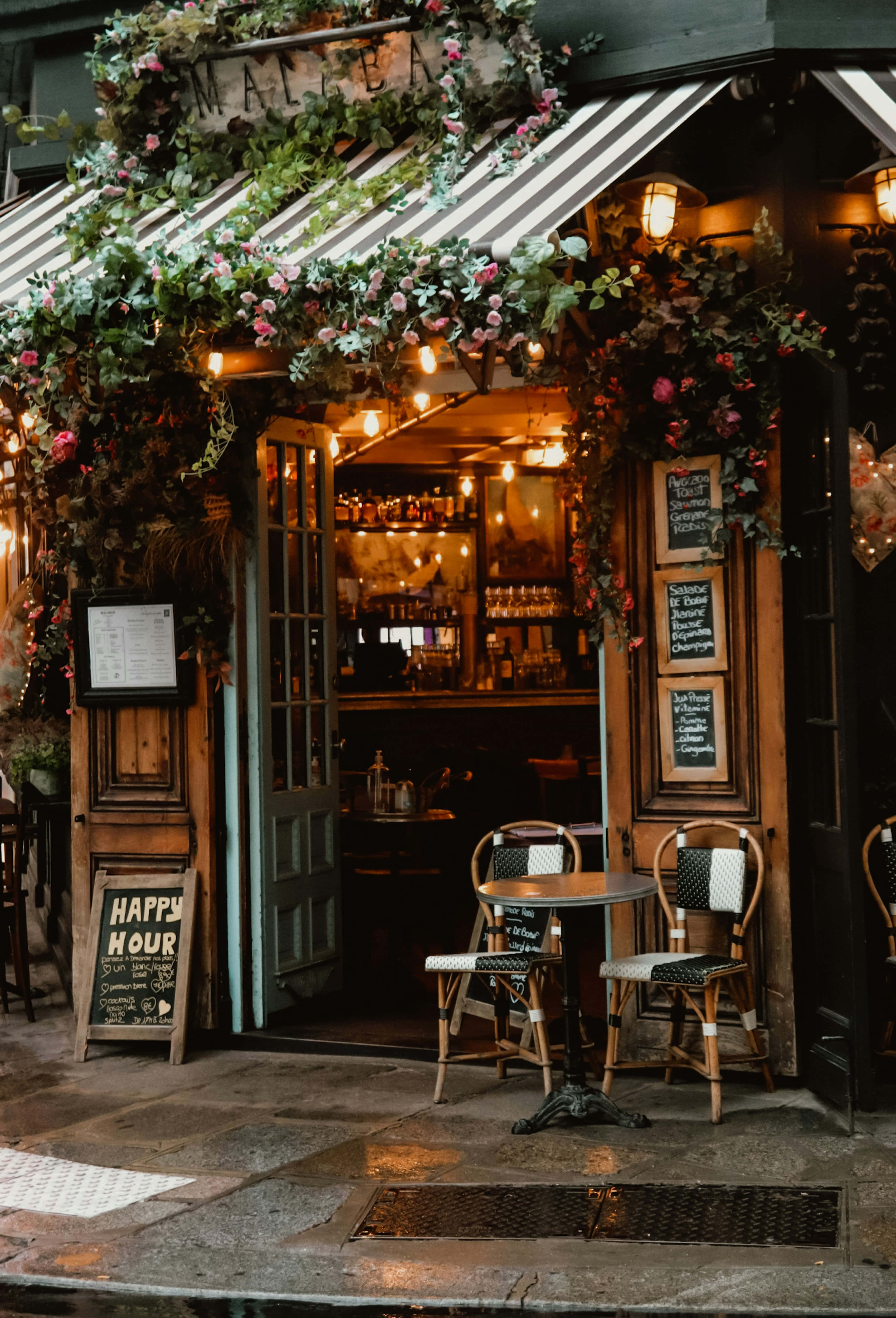 vintage cafe entrance, lush pink flowers, warm string lights, 4K Phone Wallpaper