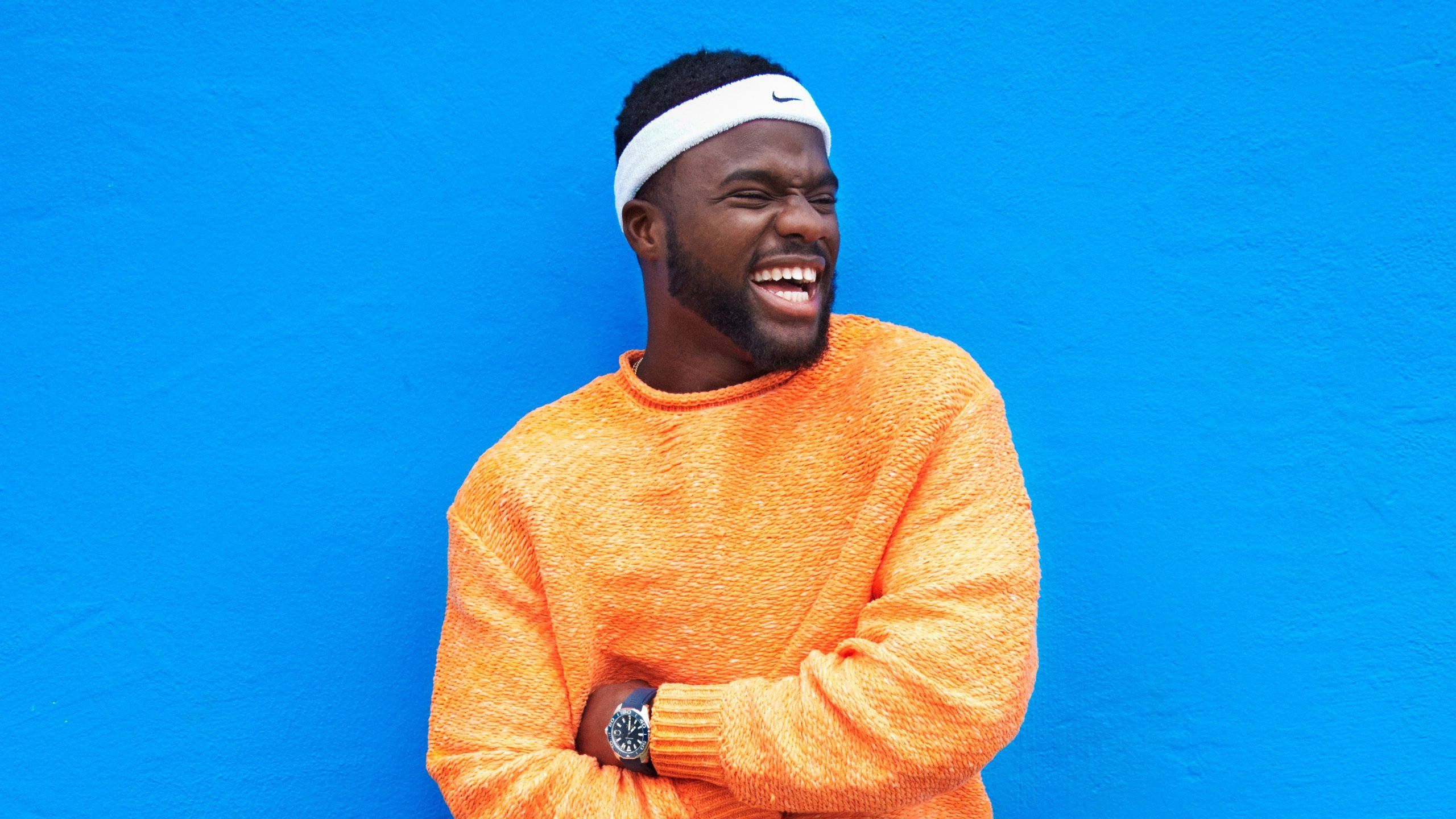 Frances Tiafoe, orange sweater, vivid blue wall, 2K Desktop Wallpaper