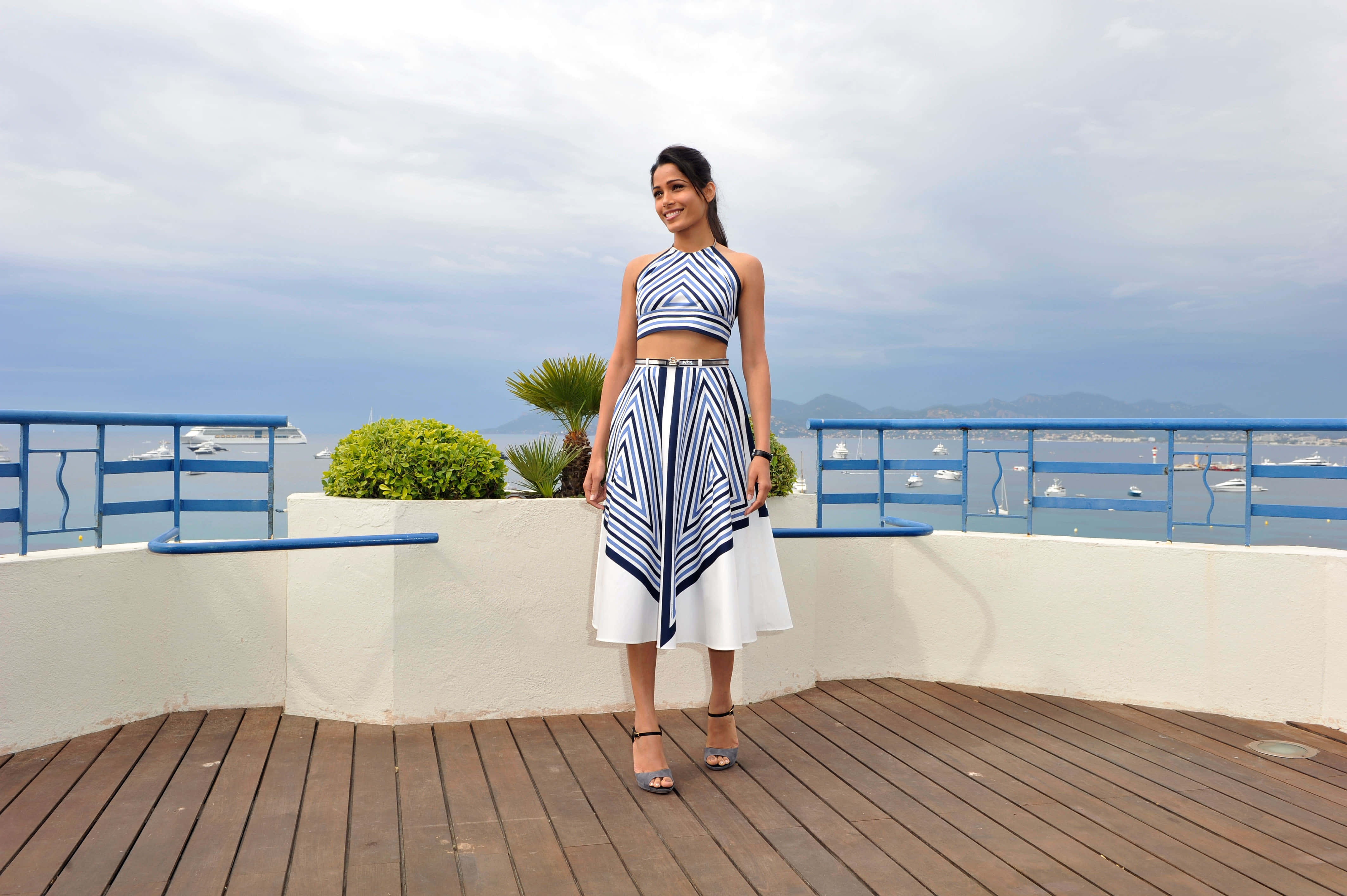 Freida Pinto, bold blue and white geometric two-piece outfit, wooden deck, 4K Desktop Wallpaper