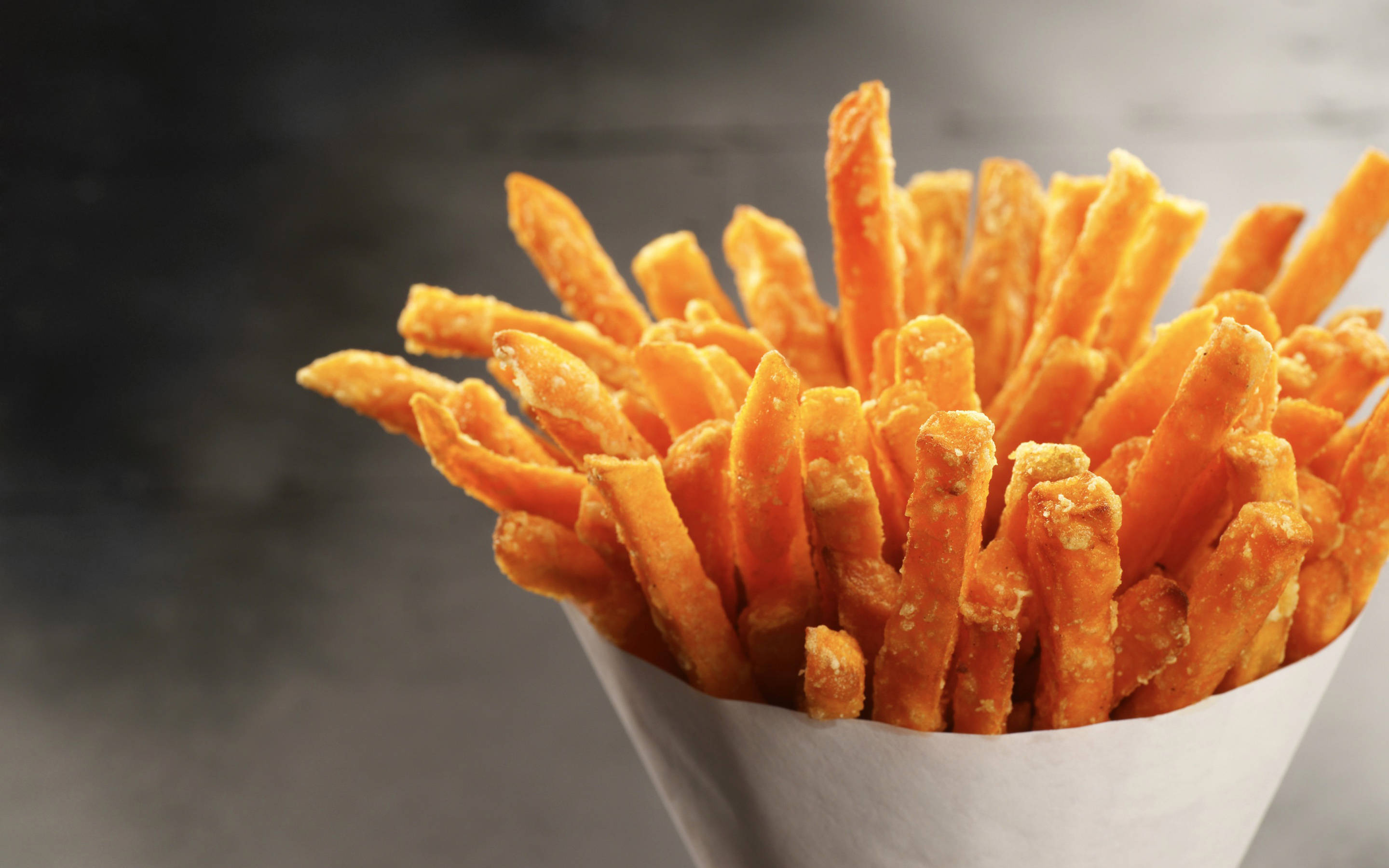 crispy sweet potato fries, white paper cone, dark blurred background, 2K Desktop Wallpaper
