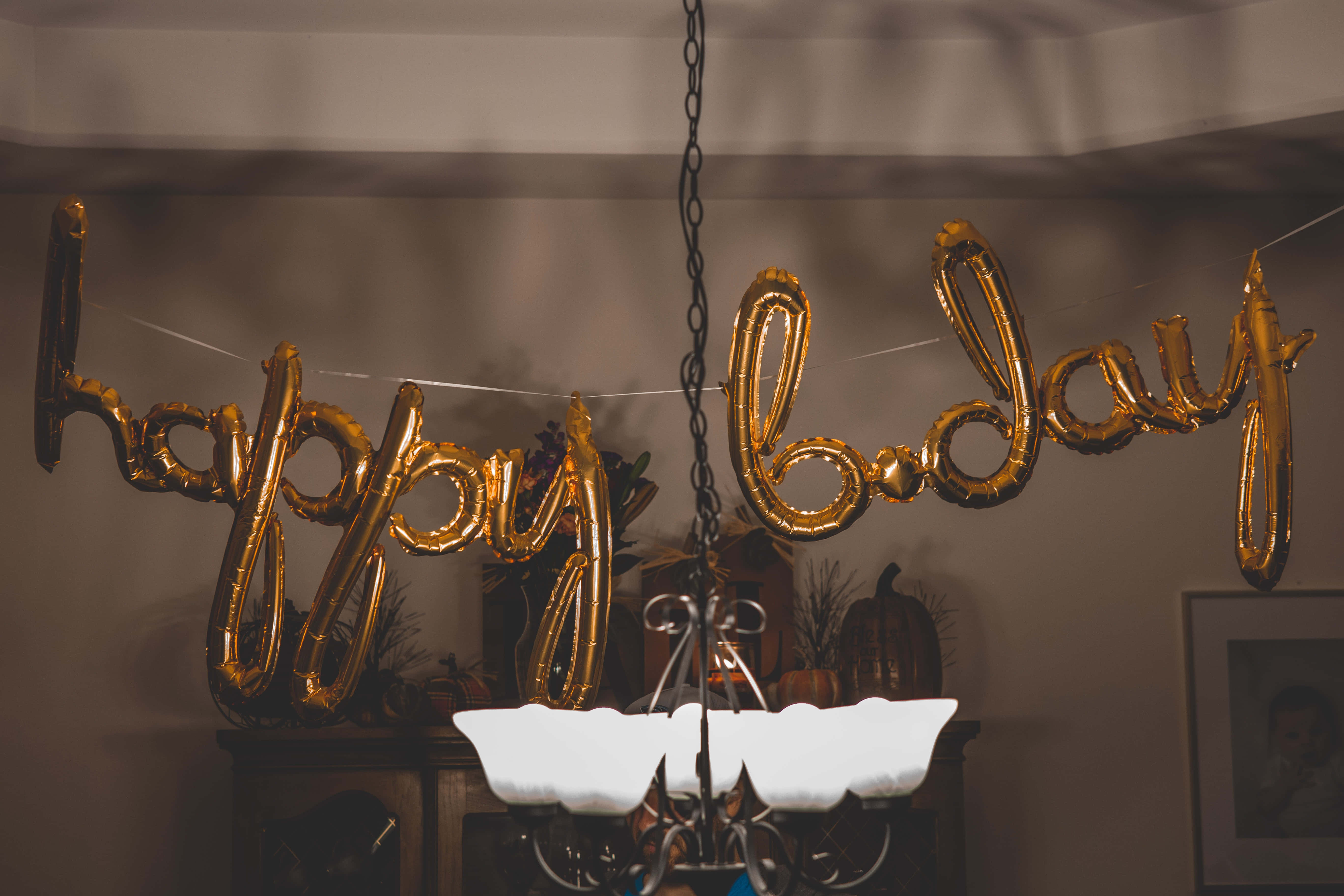 golden 'happy birthday' balloons, lit chandelier, warmly lit indoor celebration scene, 5K Desktop Wallpaper