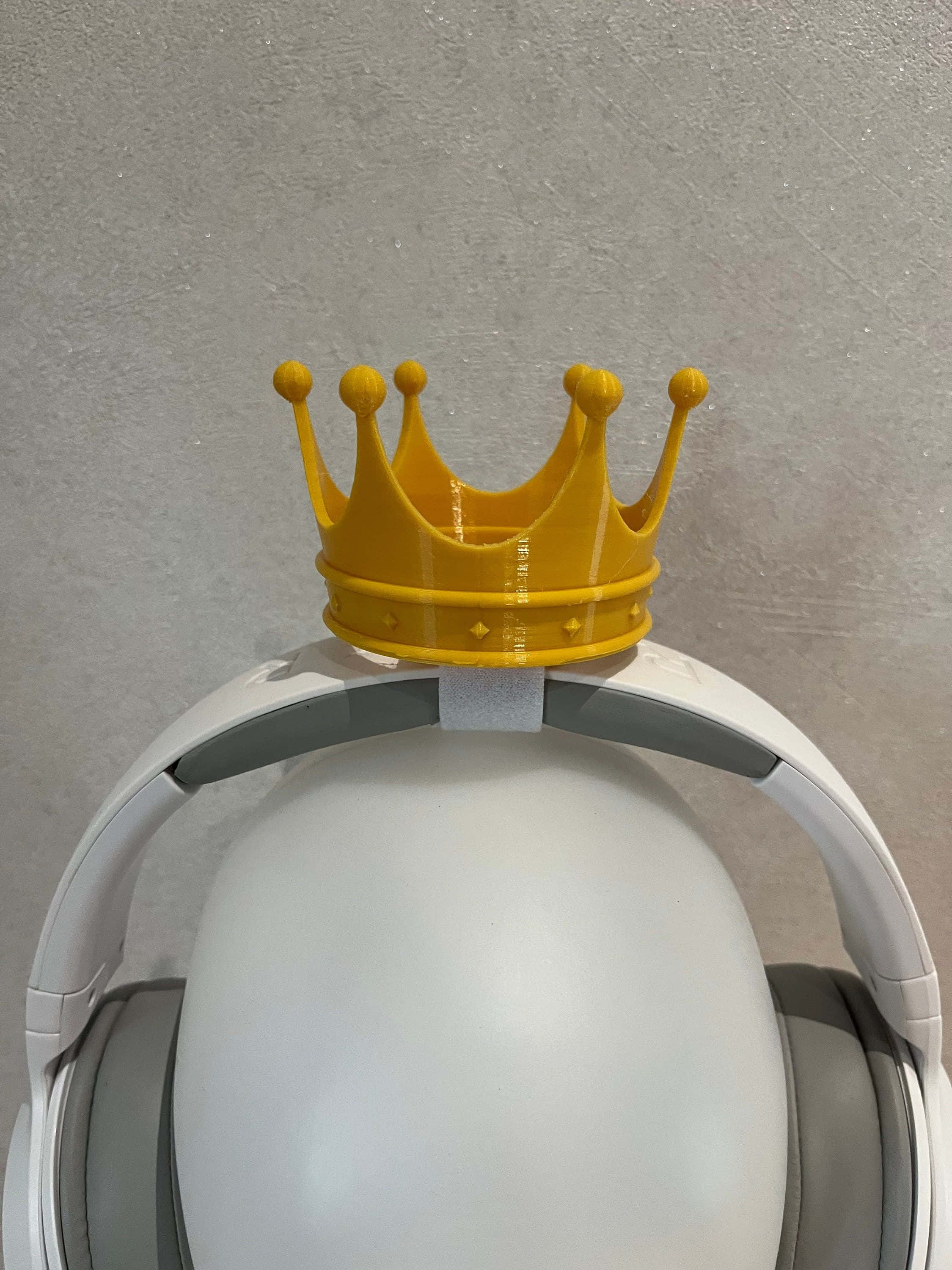 bright yellow plastic crown, white over-ear headphone, textured gray wall, 2K Phone Wallpaper