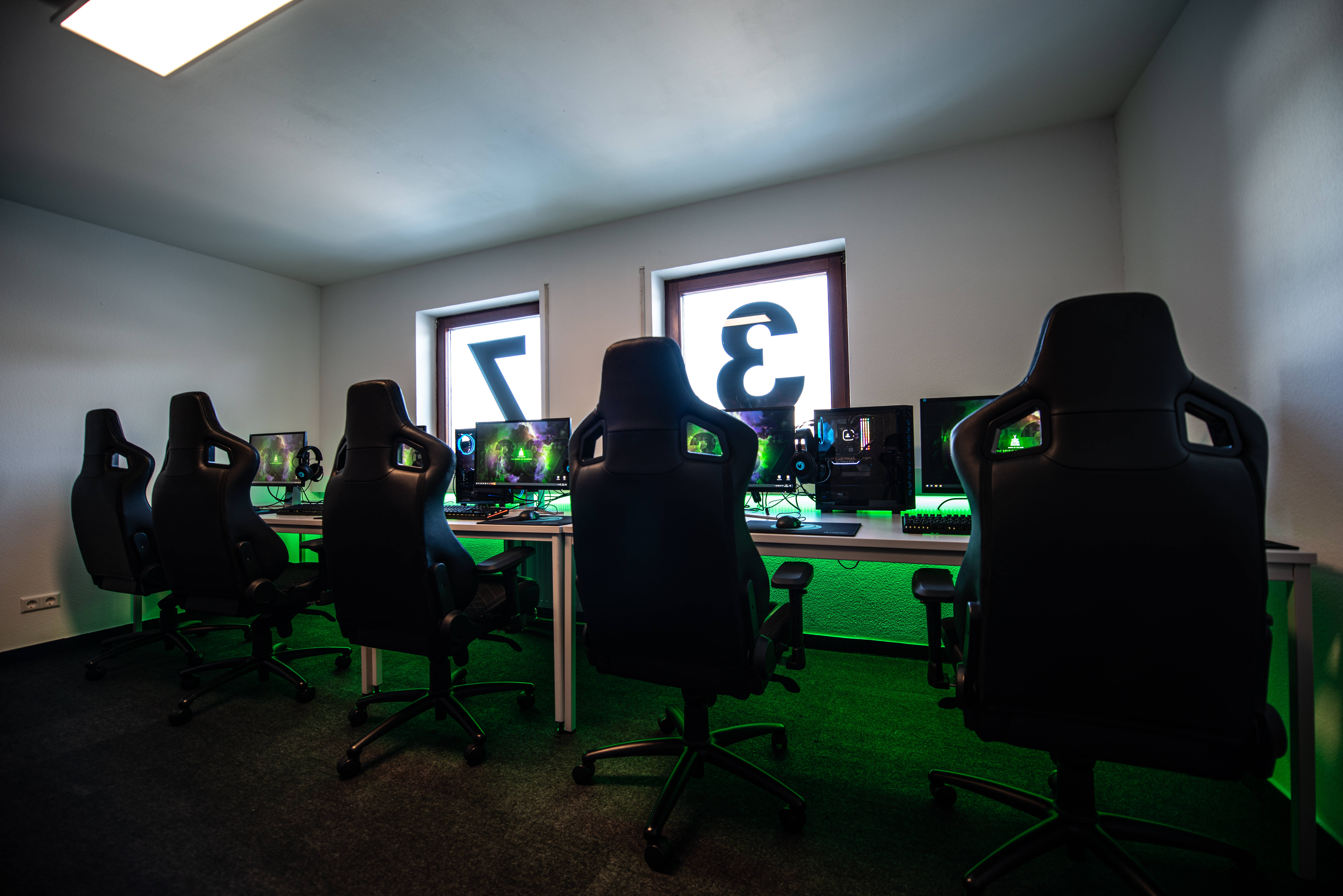 black ergonomic chairs, glowing monitors, green under-desk lighting, 5K Desktop Wallpaper