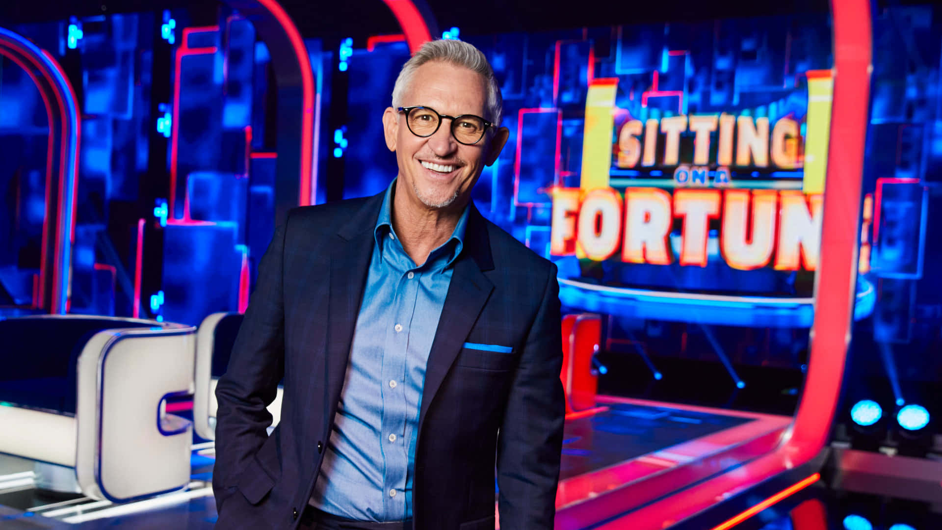 Gary Lineker, Sitting on a Fortune, vibrant blue and red game show set, Full HD Desktop Wallpaper