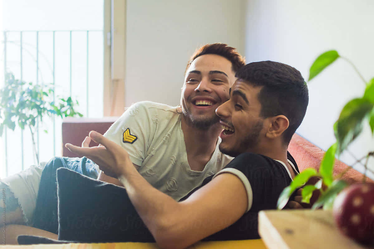 Gay Latino couple, sunlit couch, green plants, SD Desktop Wallpaper