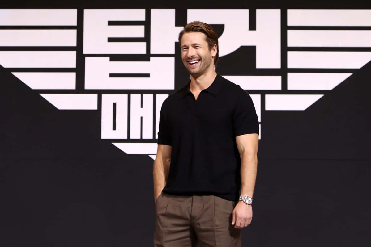 Glen Powell, black polo shirt, black and white Korean text backdrop, SD Desktop Wallpaper