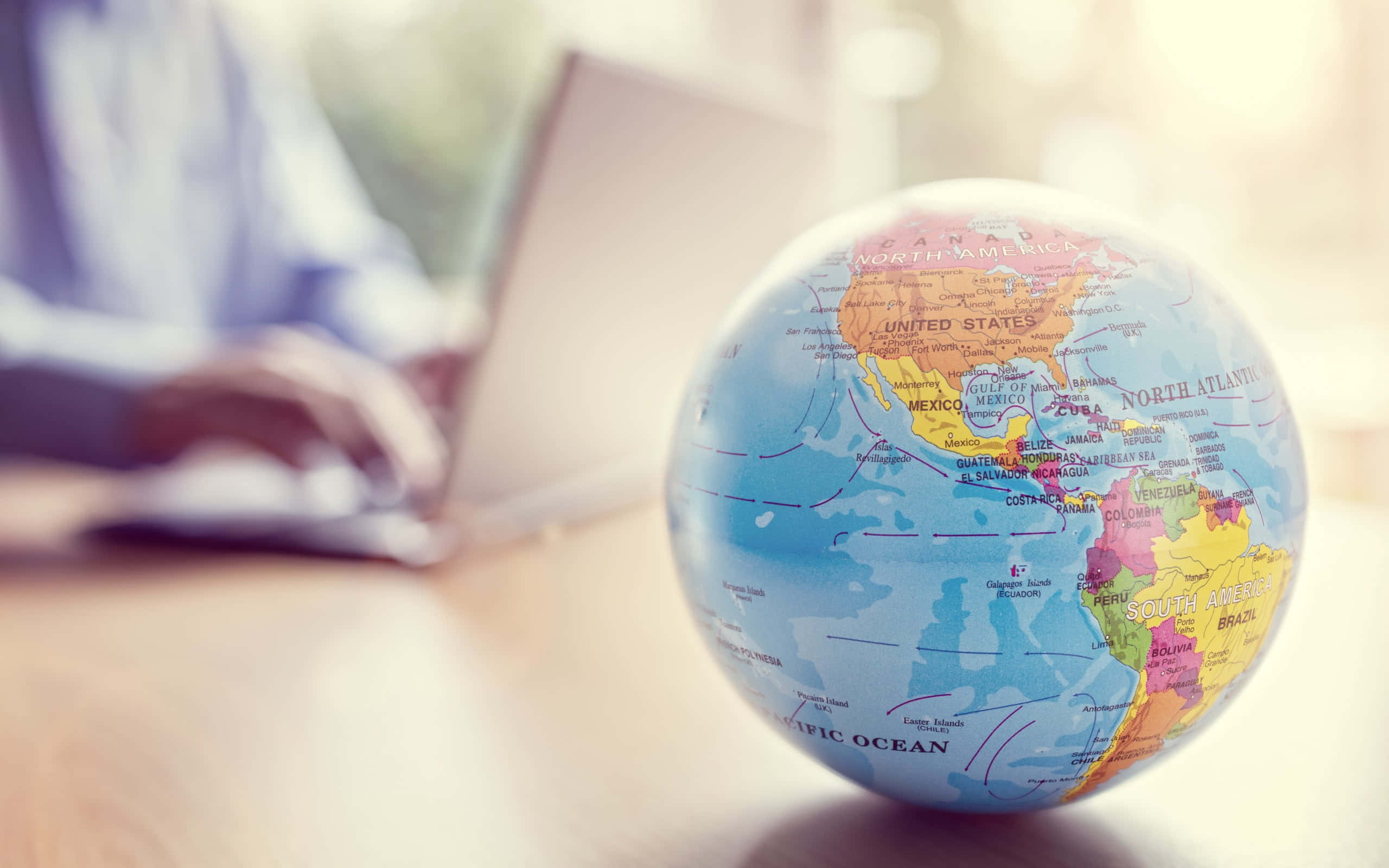 small globe map, wooden desk, blurred person, 2K Desktop Wallpaper
