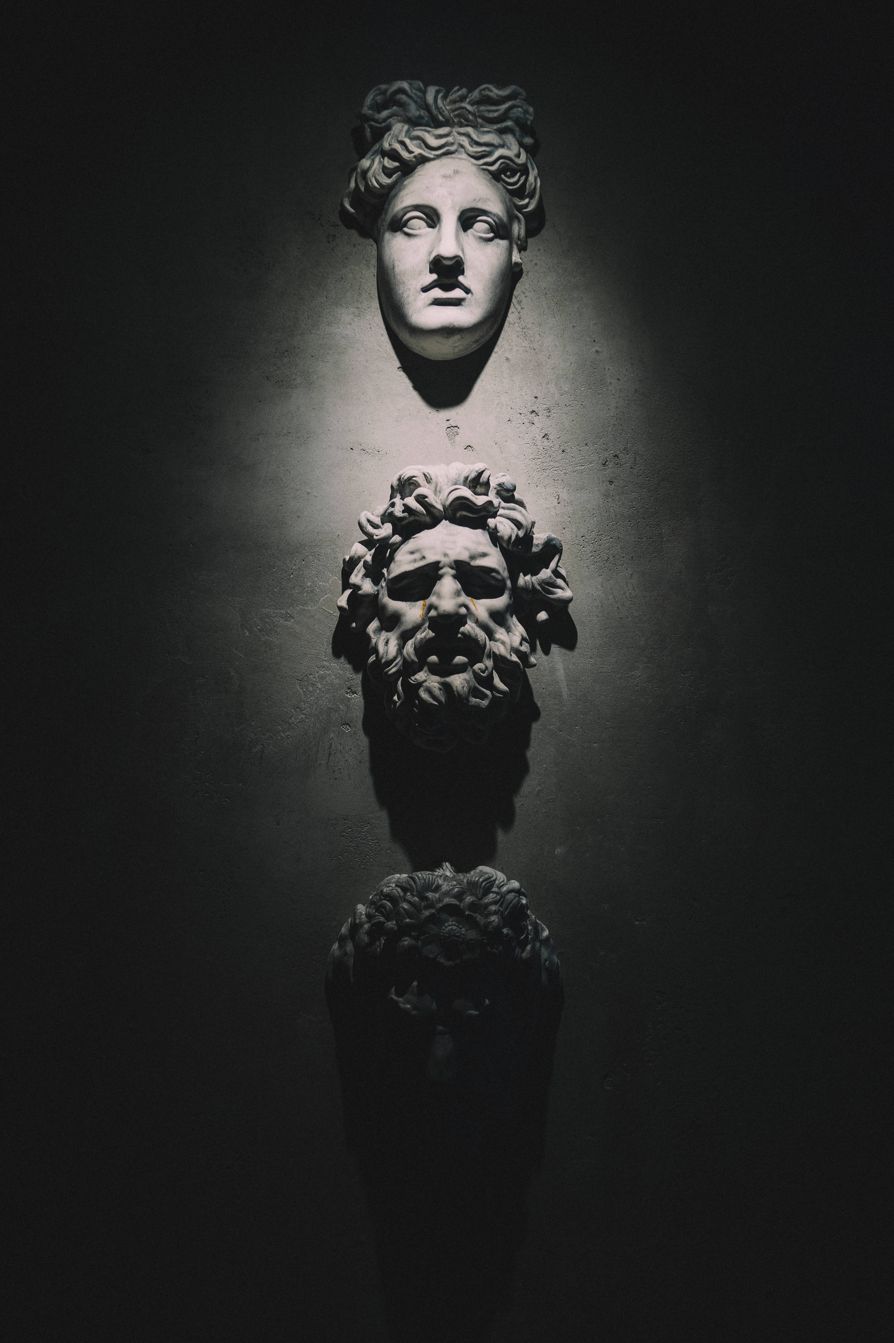 classical stone masks, dramatic spotlight, dark wall, 4K Phone Wallpaper
