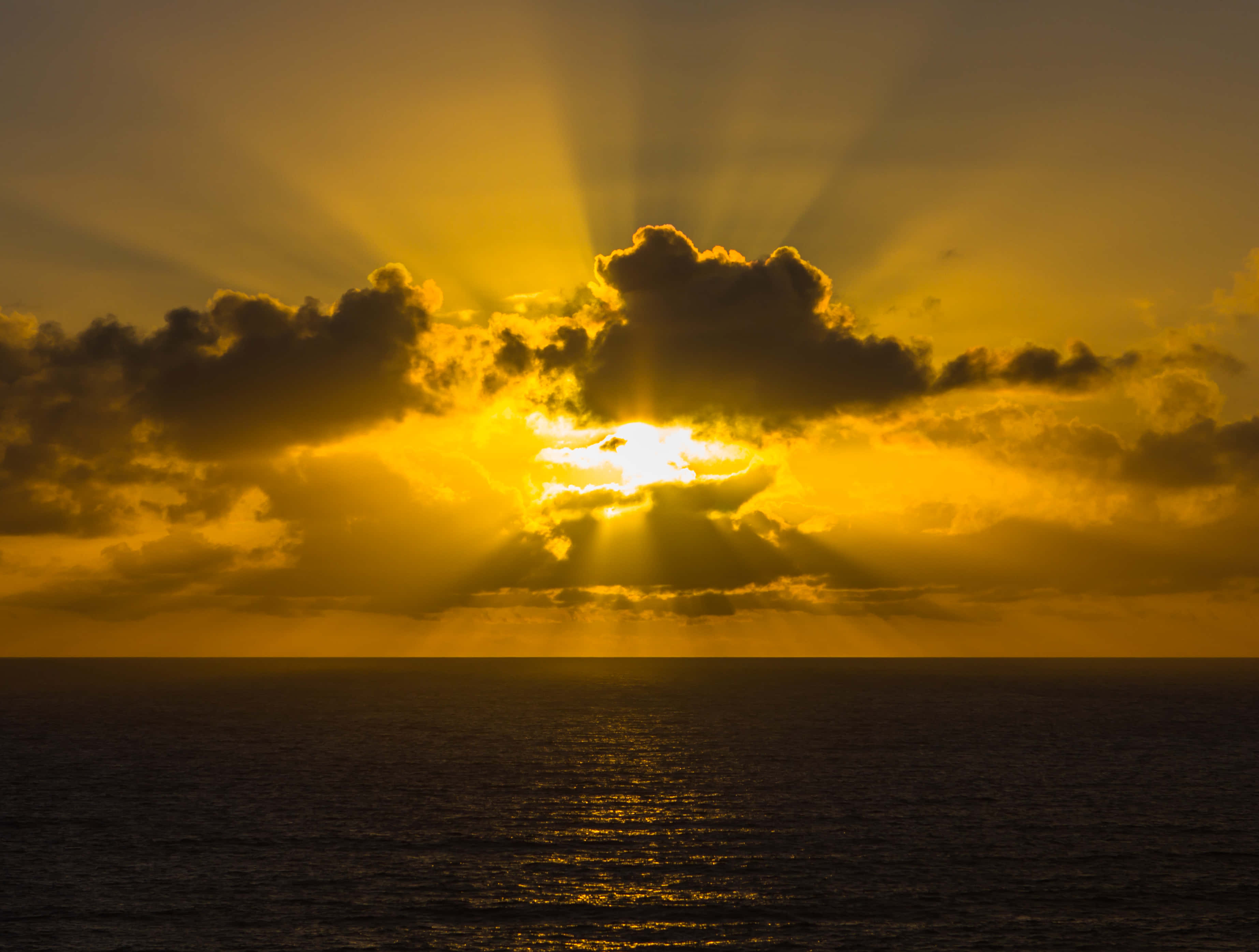 Golden sunburst, dramatic clouds, calm ocean, 2K Desktop Wallpaper