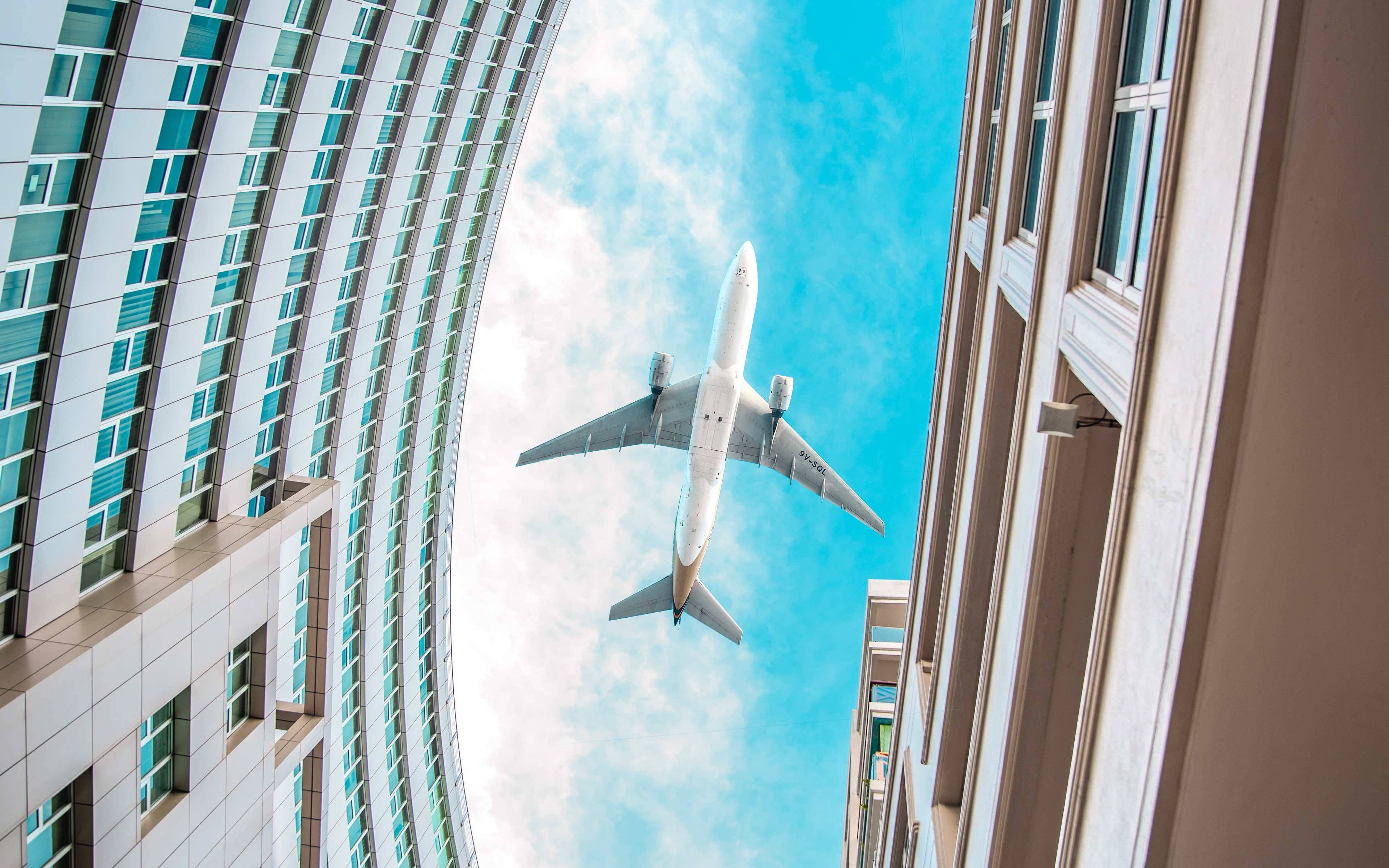 Google Flights, white airplane, towering modern buildings, 4K Desktop Wallpaper