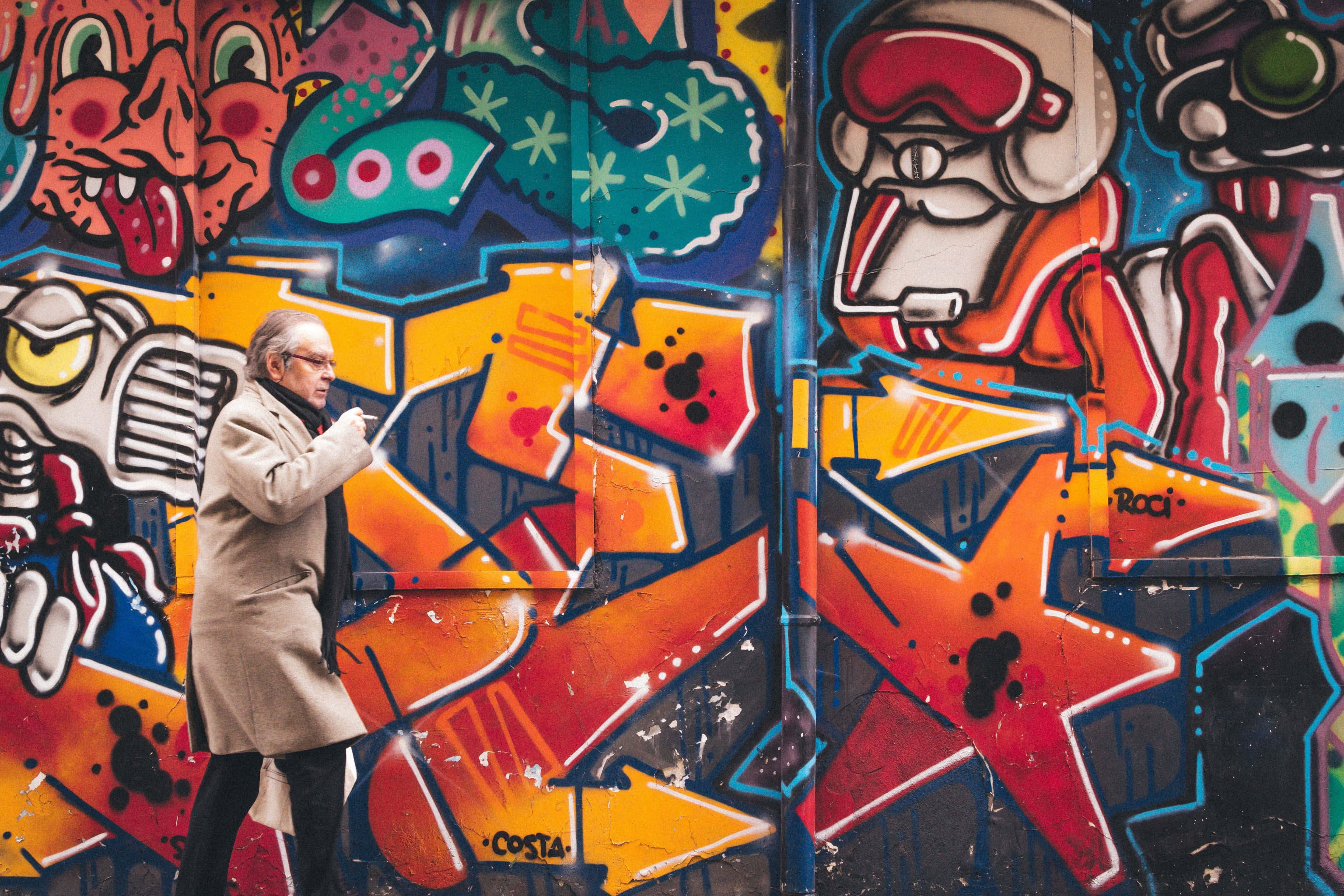 beige coat, vibrant graffiti-covered wall, cartoonish characters, 4K Desktop Wallpaper