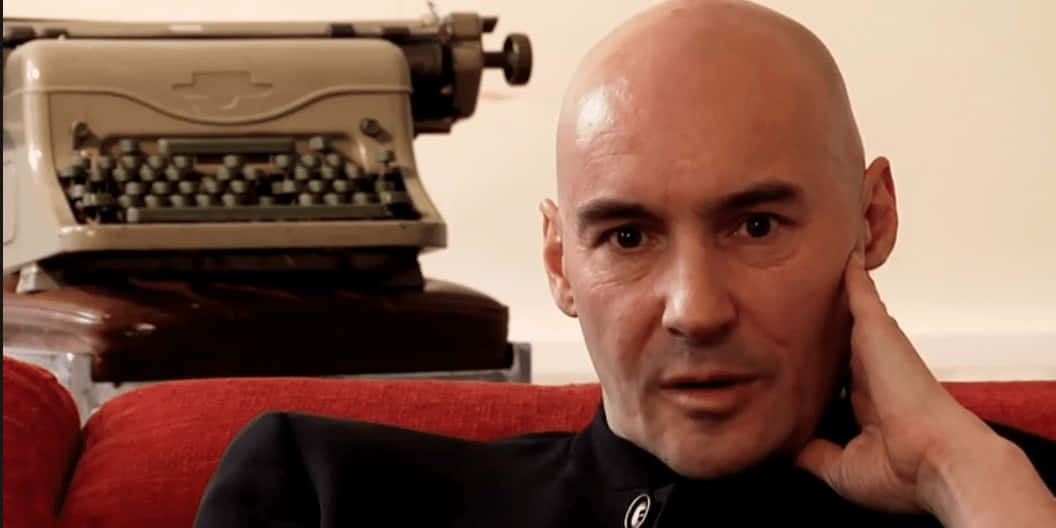 Grant Morrison, black shirt, red couch, SD Desktop Wallpaper