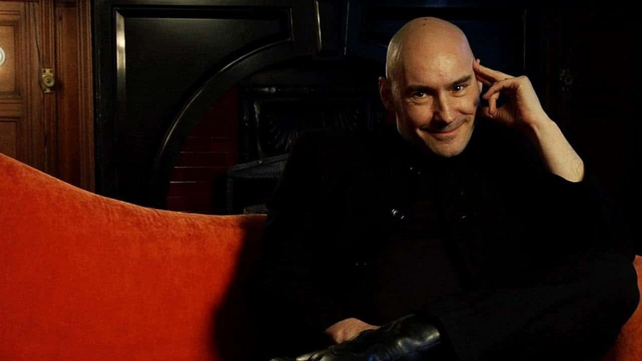 Grant Morrison, black suit, plush red couch, SD Desktop Wallpaper