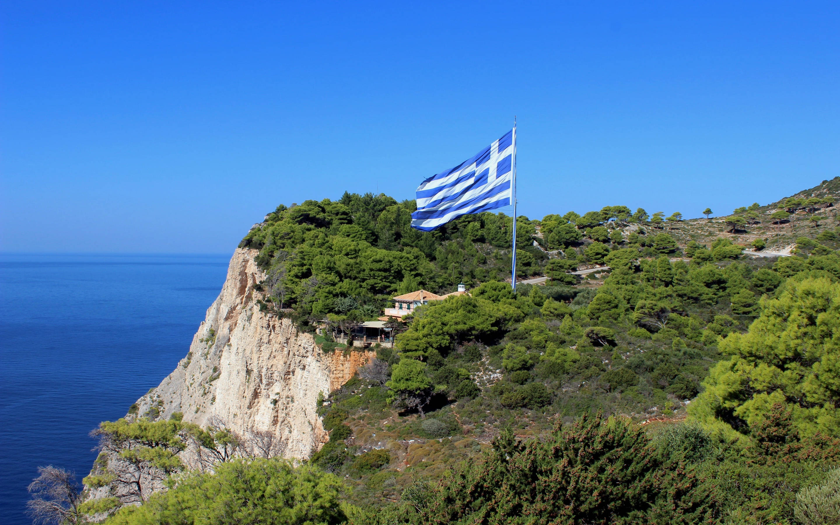 Greek flag, sunlit cliff, deep blue Aegean Sea, 2K Desktop Wallpaper