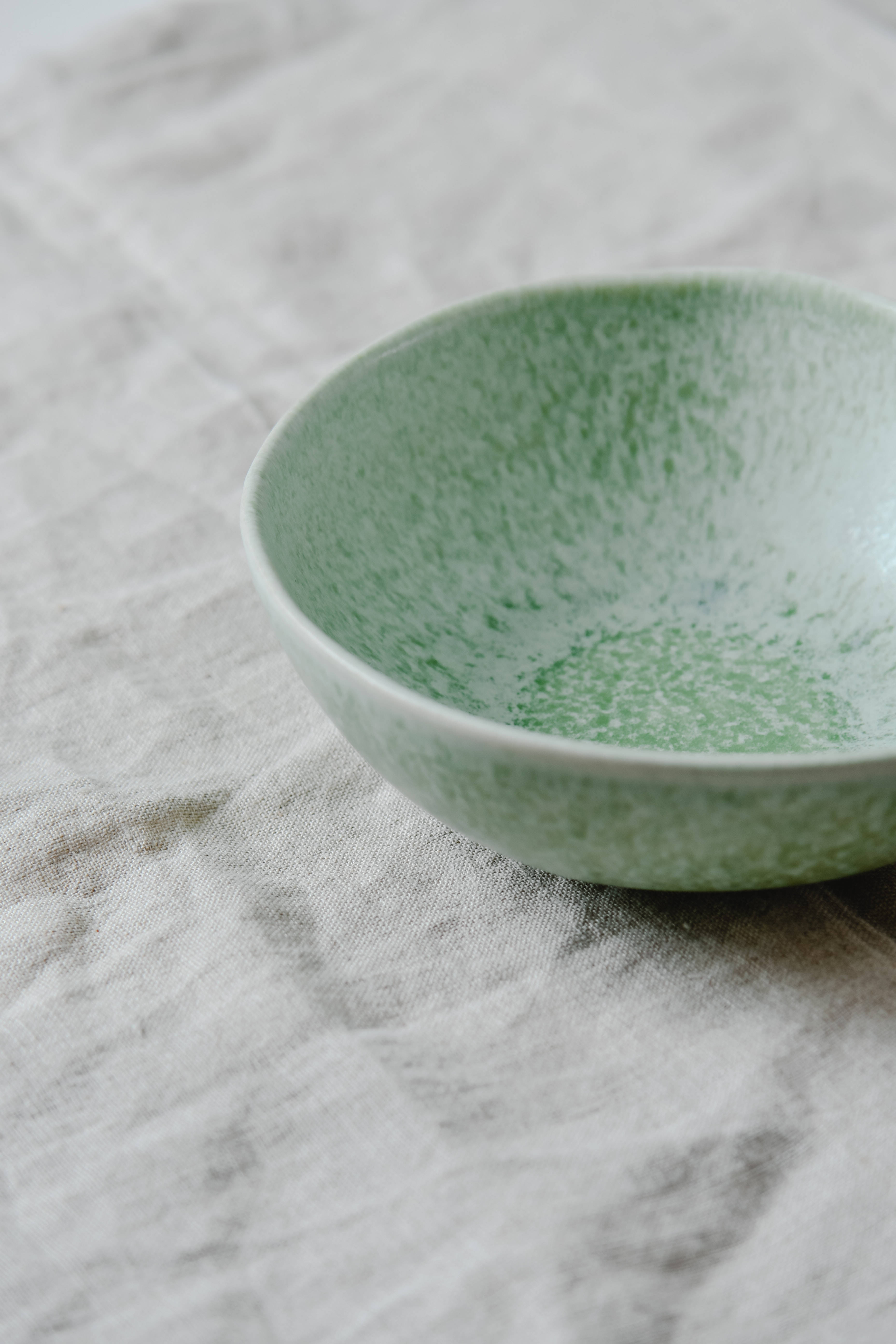 aesthetic green minimalist bowl, speckled light green ceramic bowl, textured off-white linen surface, 5K Phone Wallpaper