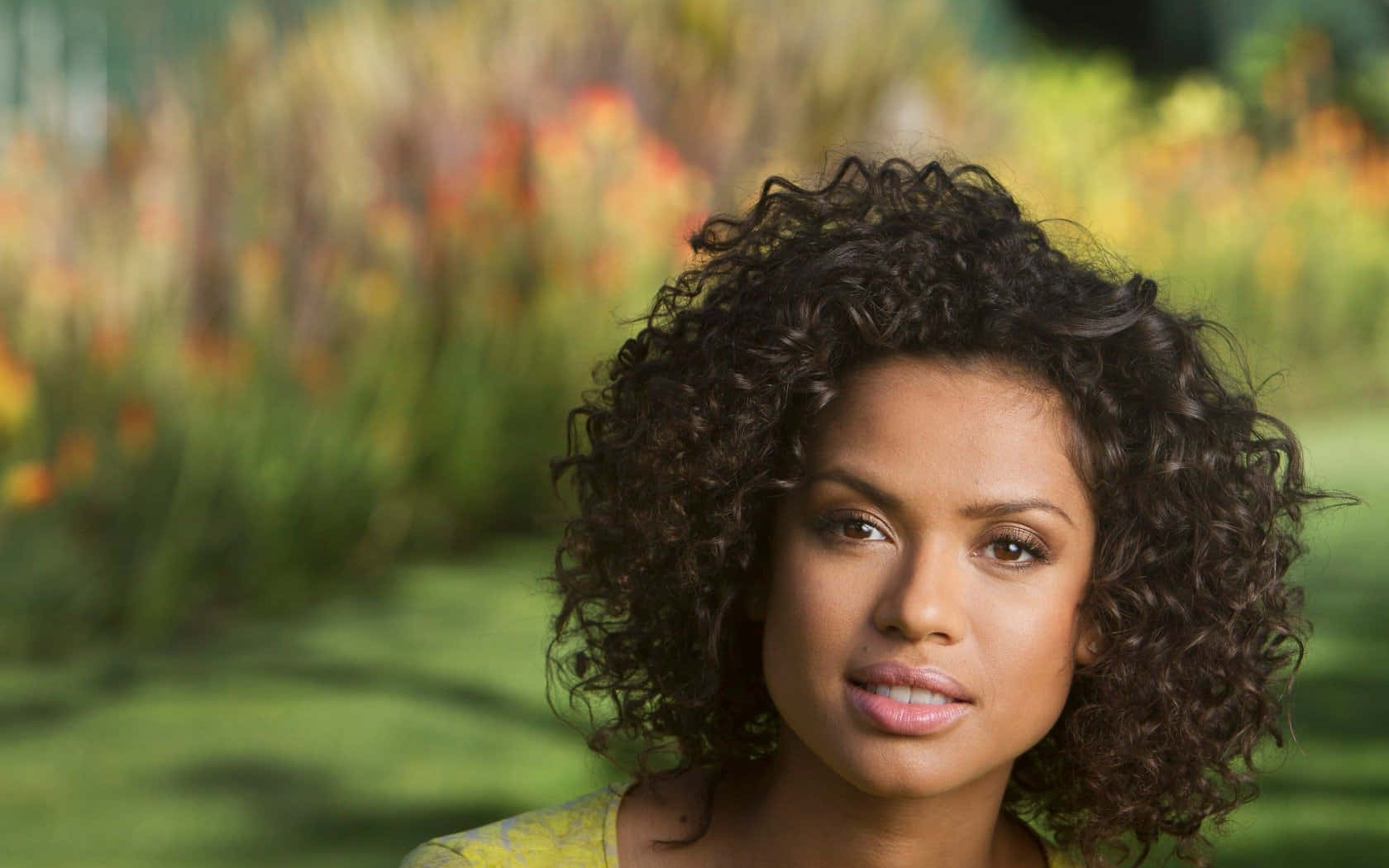 Gugu Mbatha-Raw, dark curly hair, vibrant blurred garden backdrop, HD Desktop Wallpaper