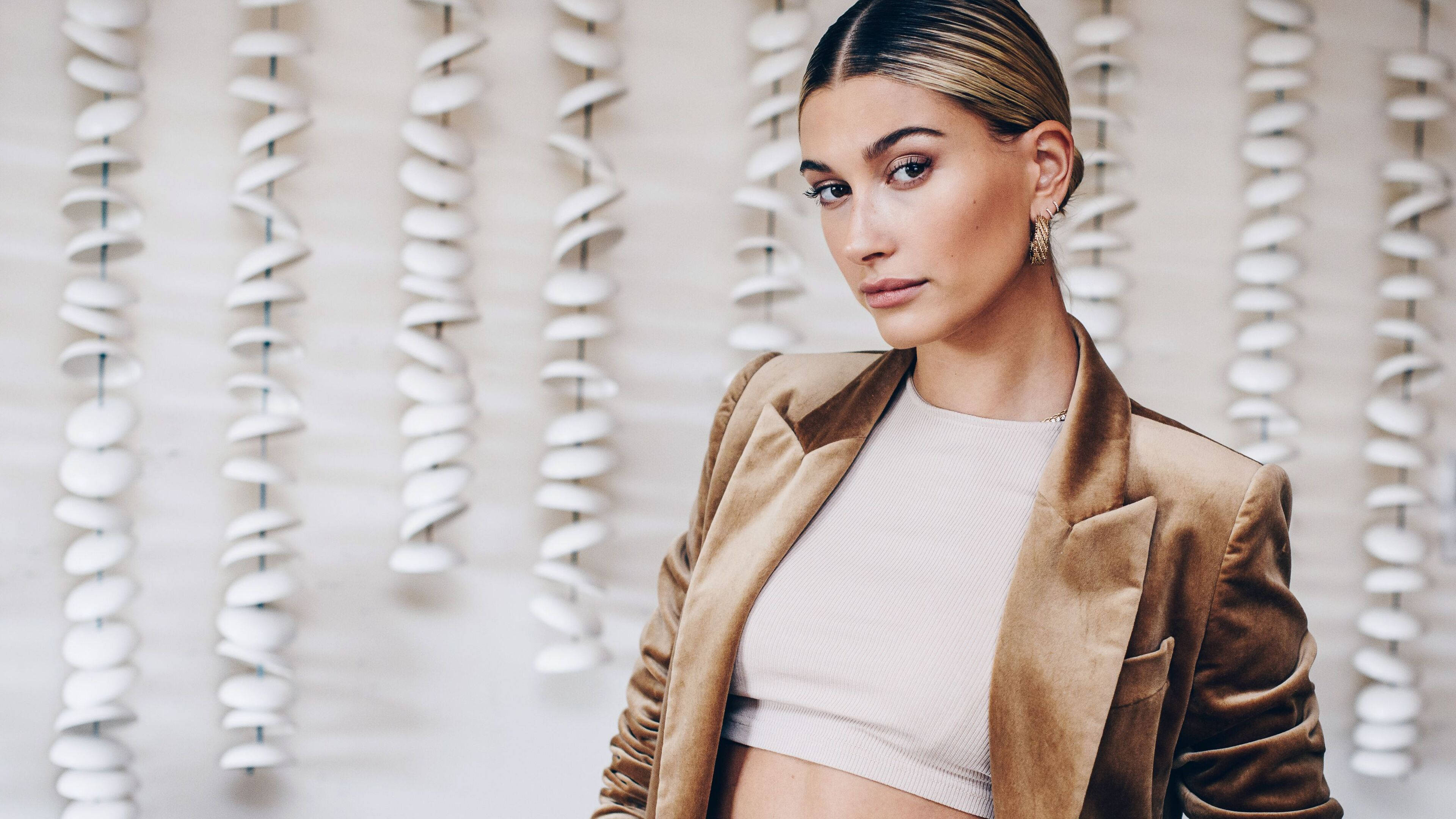 Hailey Bieber, brown velvet blazer, vertical white spiral sculptures, 4K Desktop Wallpaper