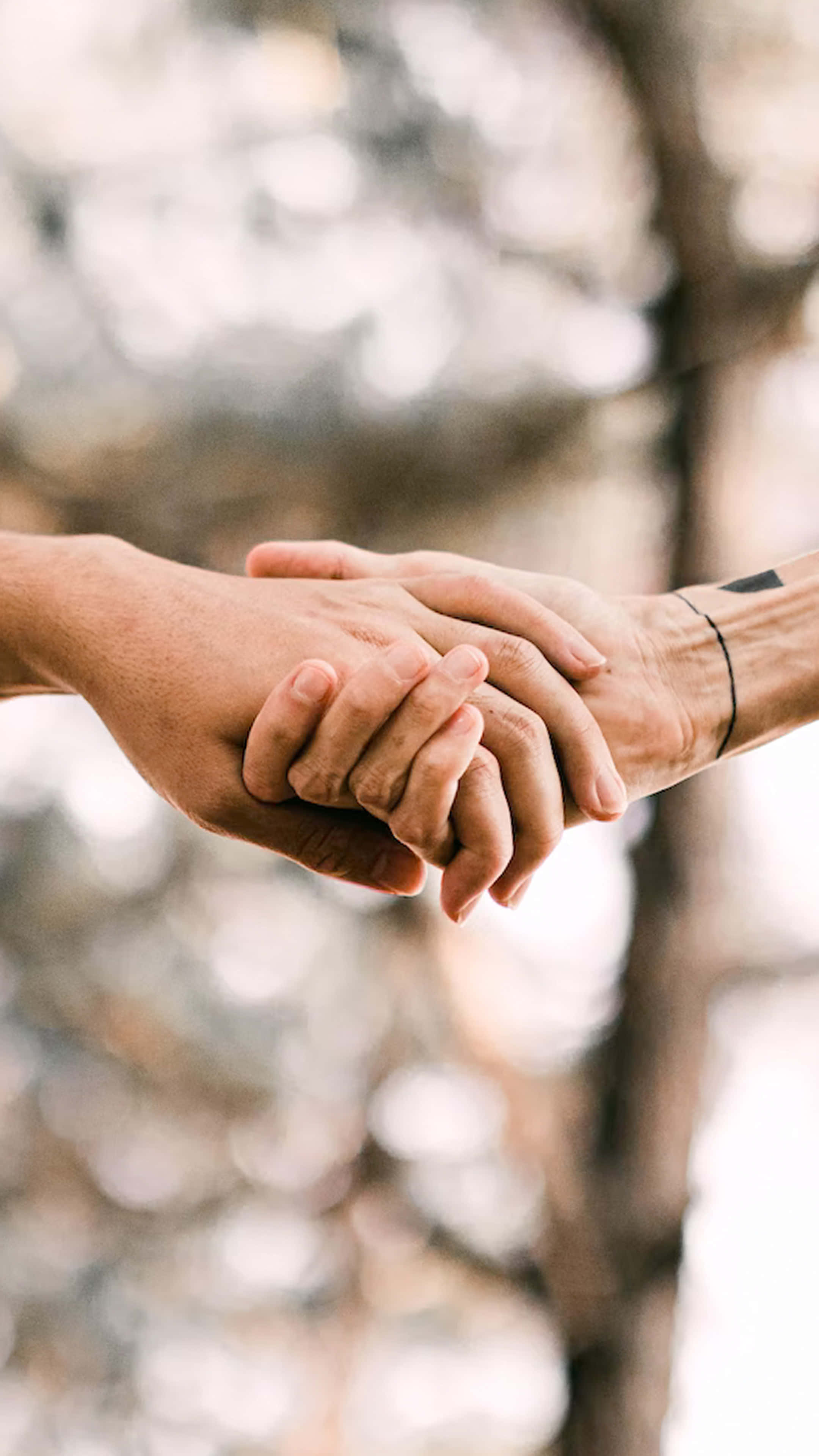 Handshake With Tattoos Outdoors, tender outdoor embrace, soft blurred forest backdrop, 4K Phone Wallpaper