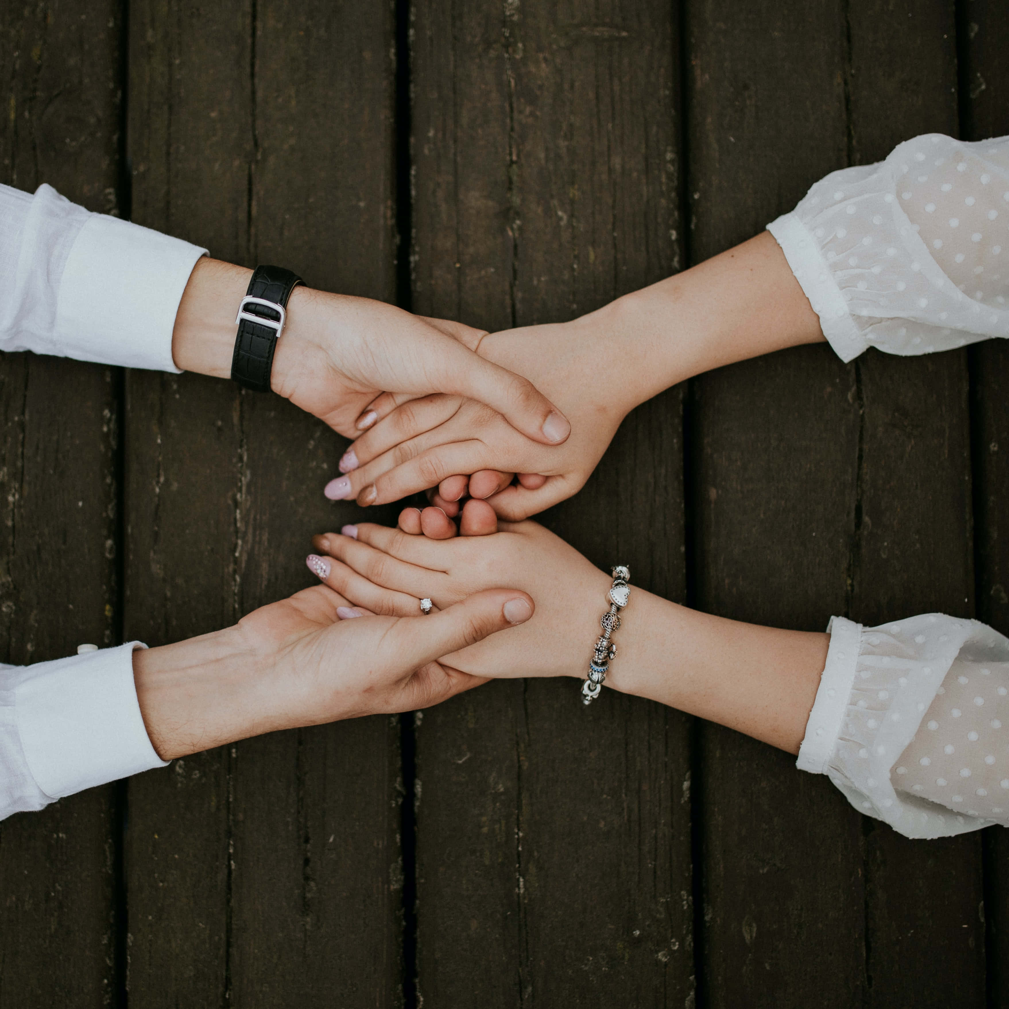 compassionate hands together, four hands interlocked in a circle, weathered wooden planks, 2K Desktop Wallpaper