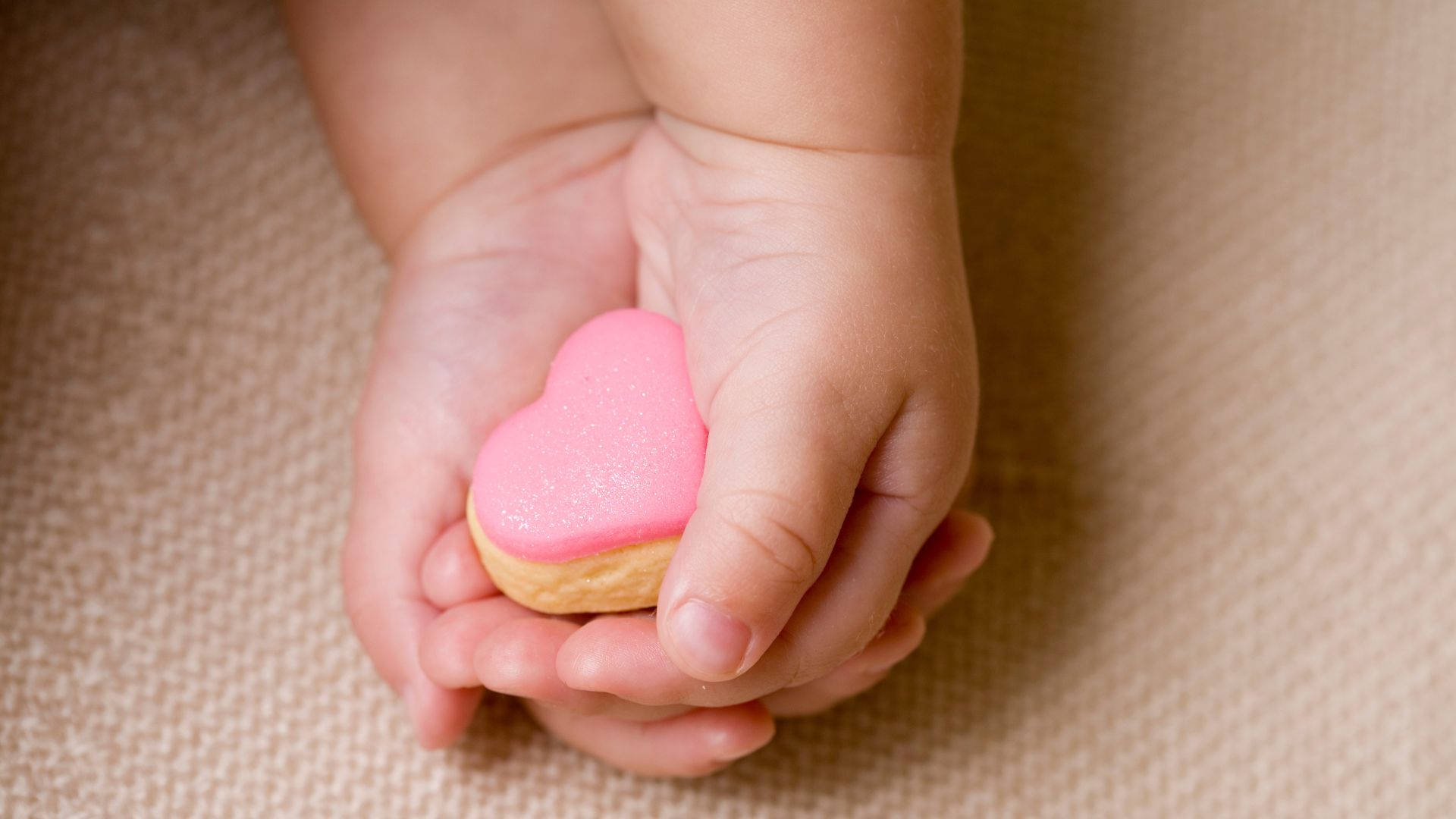 baby hands, pink-frosted heart-shaped cookie, soft beige textured background, Full HD Desktop Wallpaper
