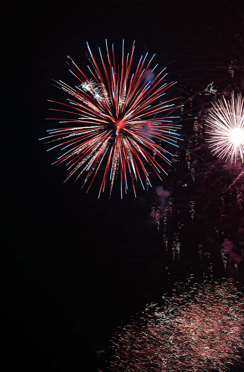 Vibrant red and blue fireworks, dark night sky, glittering water surface, SD Phone Wallpaper