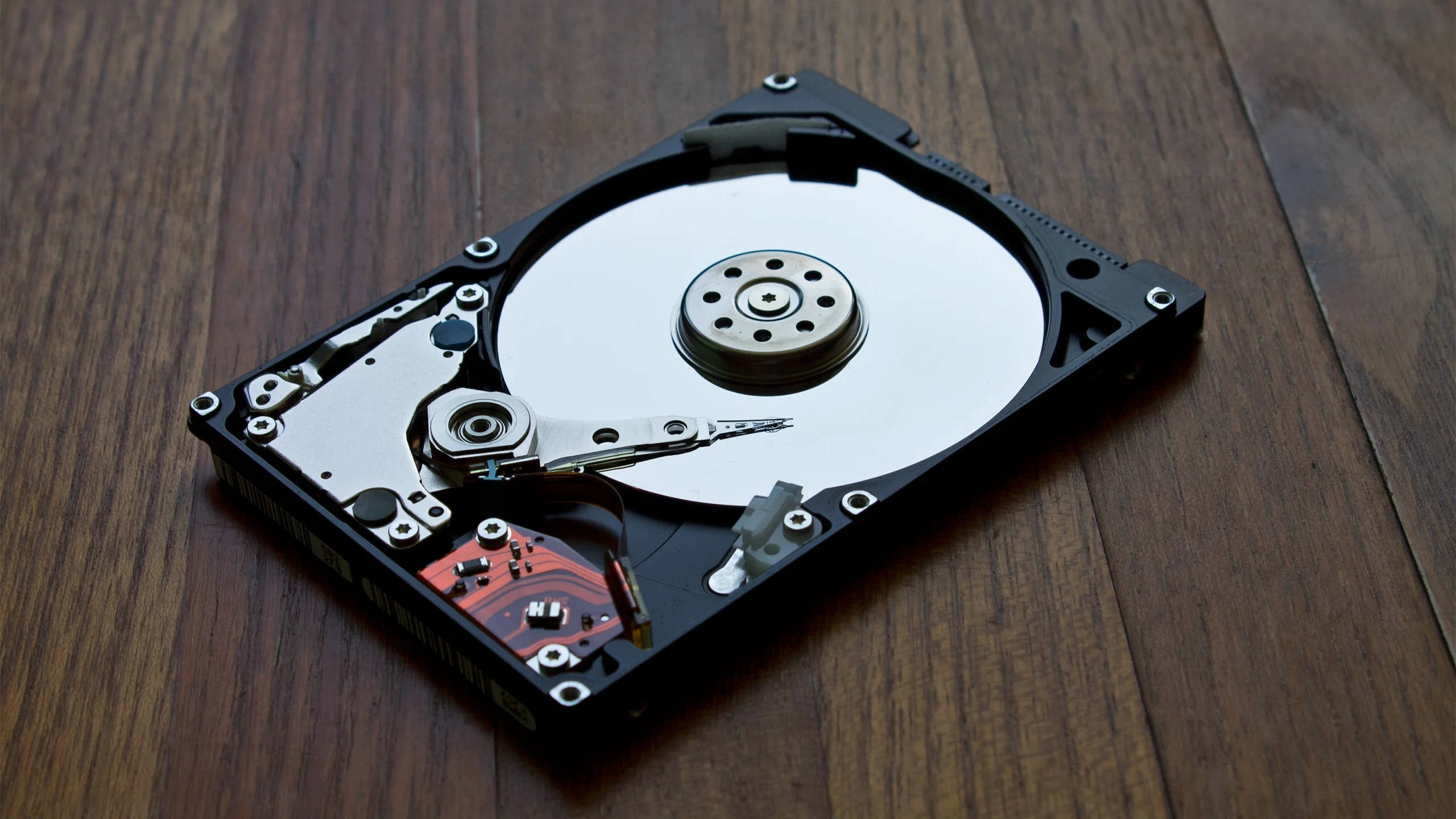 internal computer hard drive, disassembled hard disk drive, dark wooden surface, 2K Desktop Wallpaper