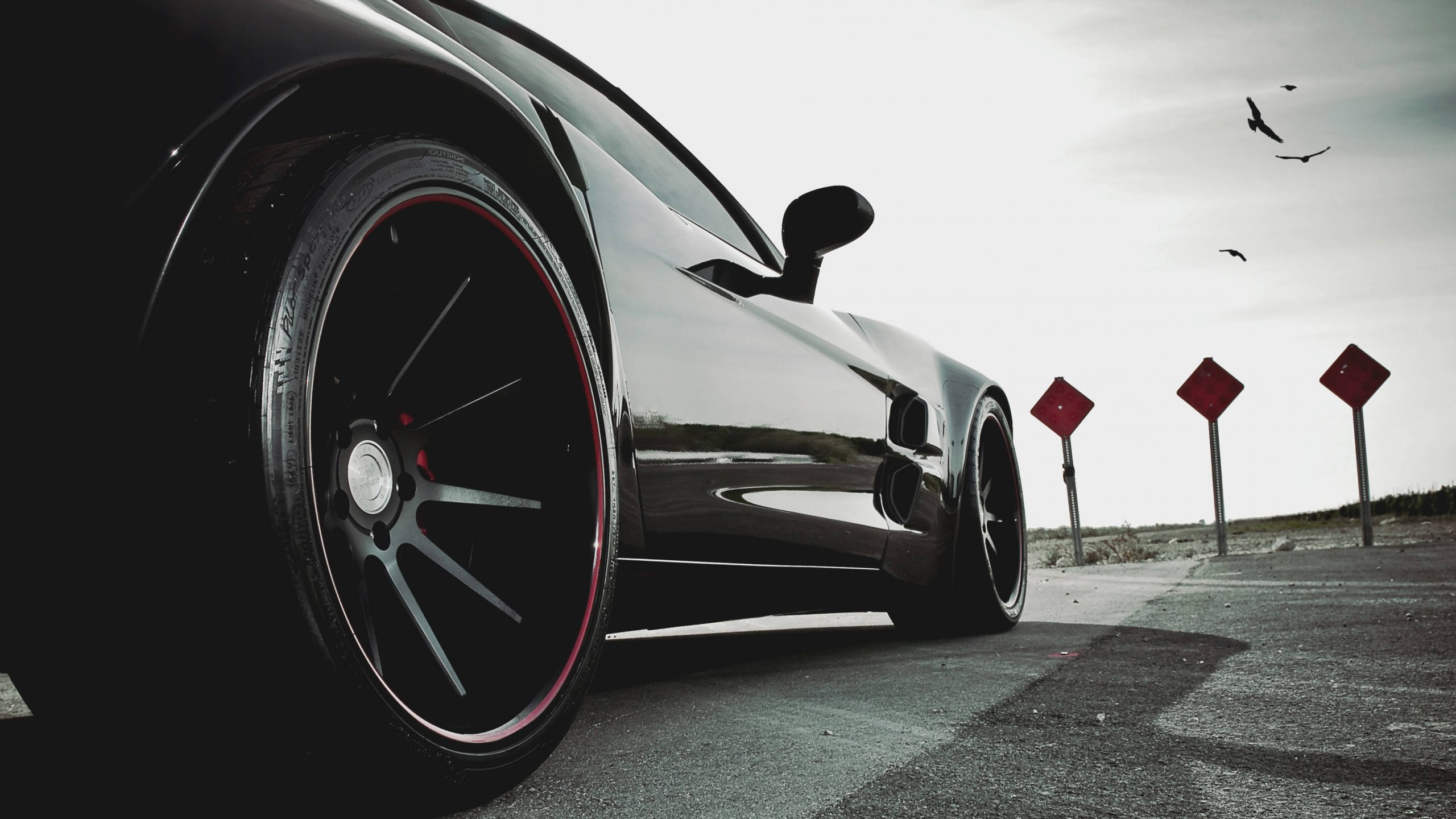 sleek black sports car, red-accented wheels, empty road, 2K Desktop Wallpaper