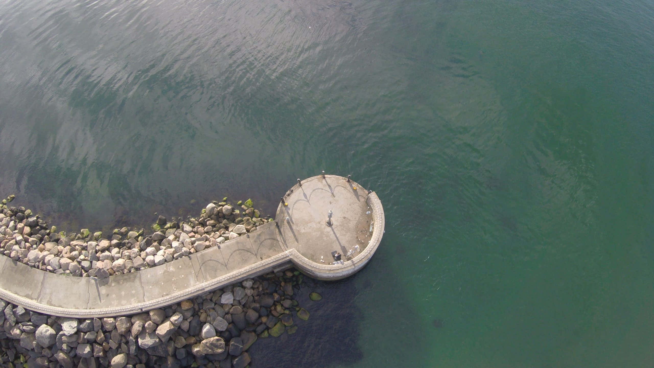curved concrete pier, calm greenish water, rocks lining its edge, 2K Desktop Wallpaper