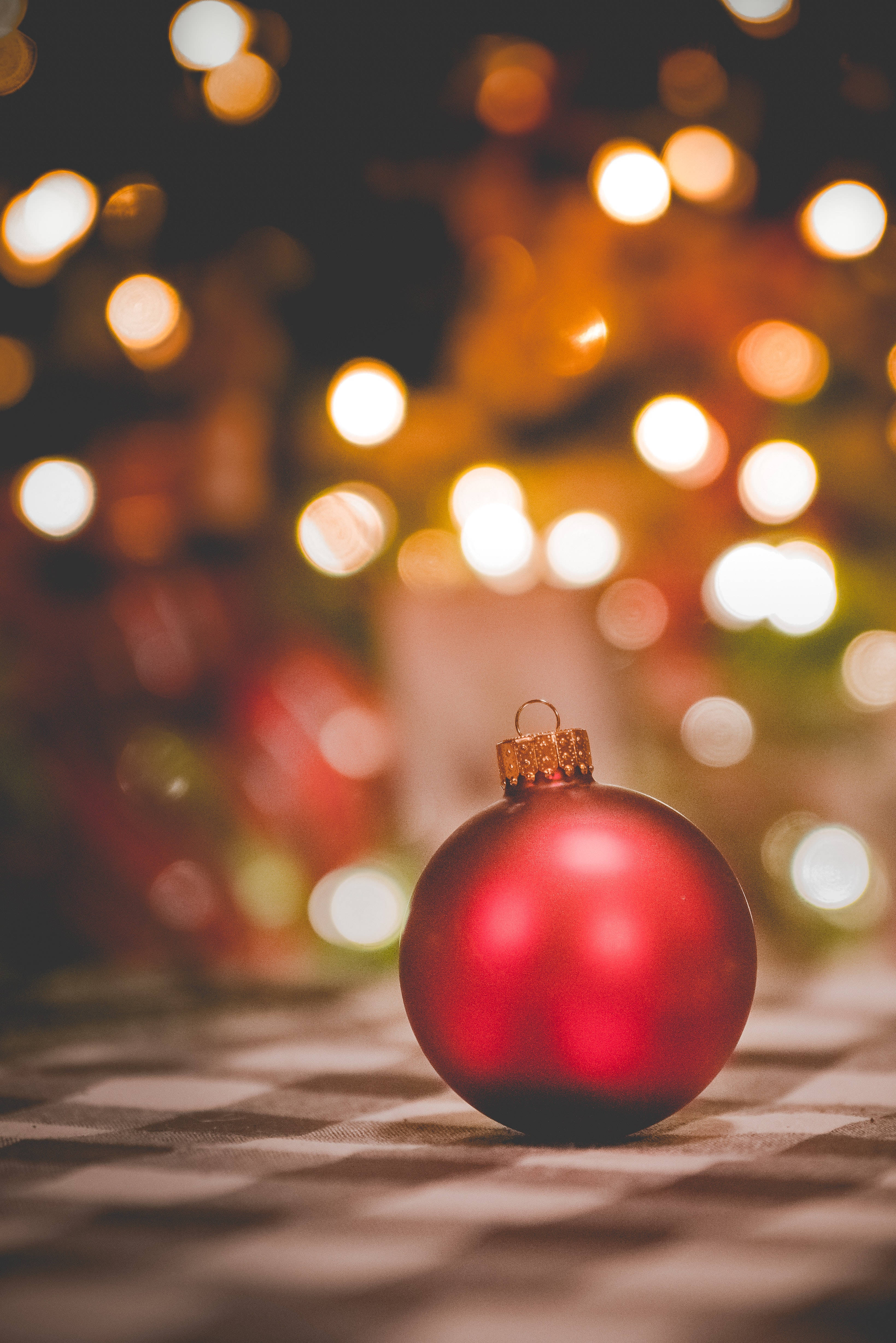 glossy red Christmas ornament, checkered surface, warm bokeh lights, 4K Phone Wallpaper