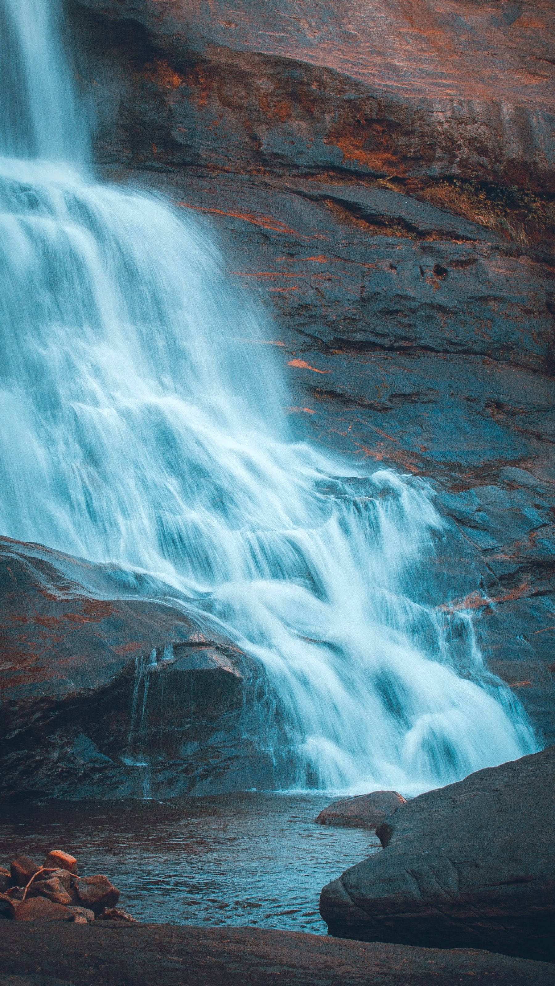 Rushing Waterfalls, dark rocks, warm orange highlights, 2K Phone Wallpaper
