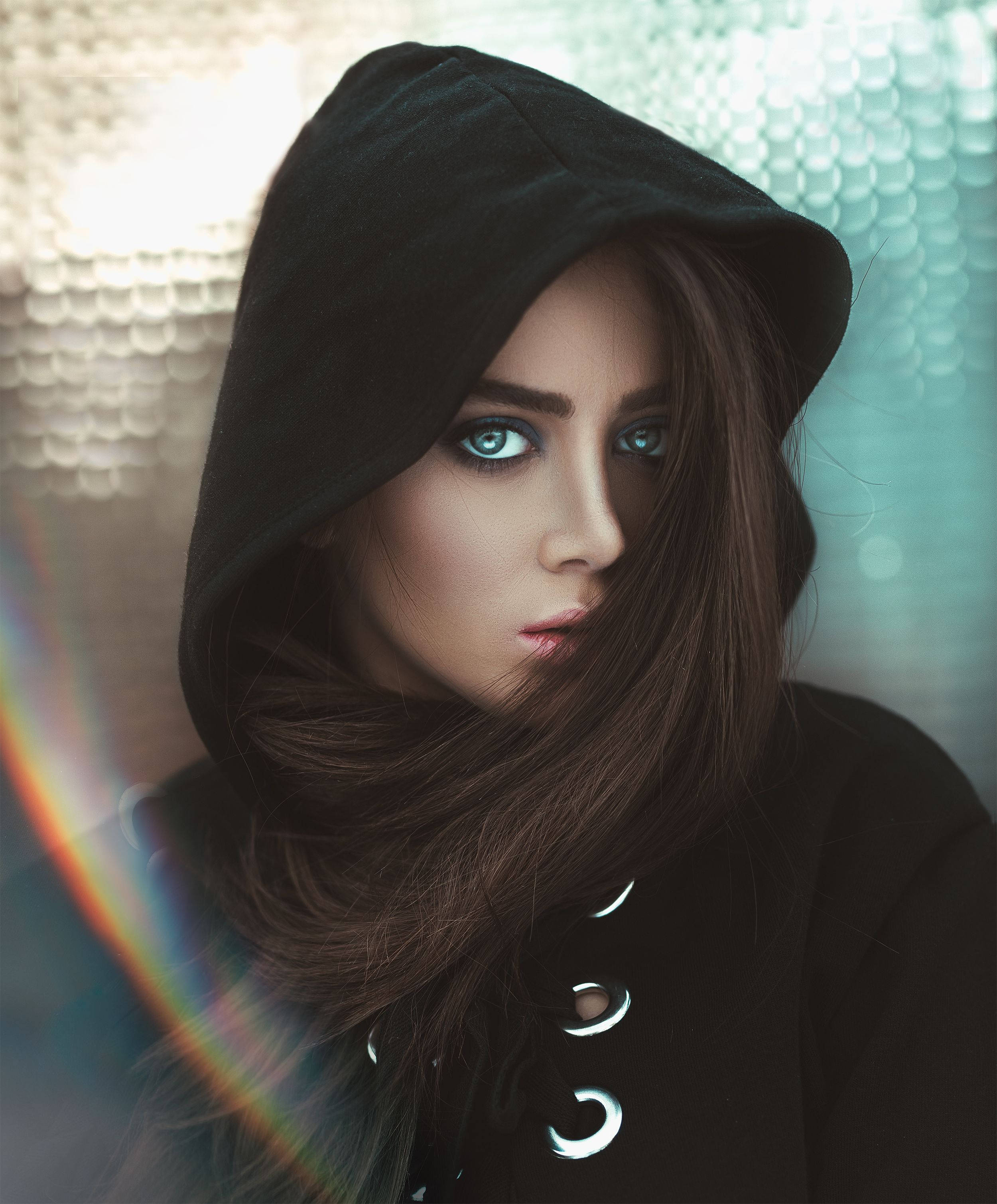 black hooded coat, striking blue eyes, textured teal and gold background, 2K Phone Wallpaper