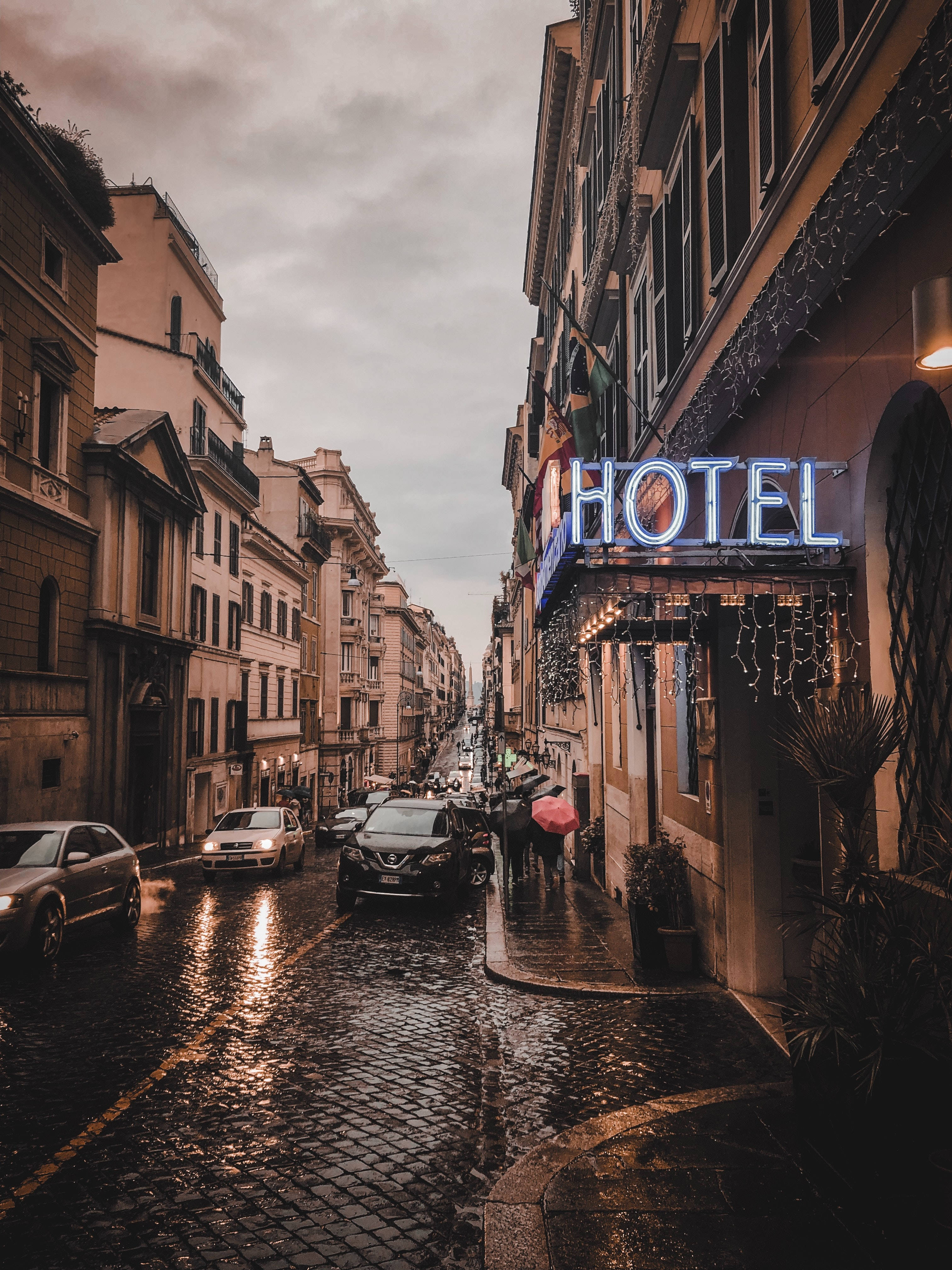 rainy cobblestone street, European city, glowing blue hotel sign, 4K Phone Wallpaper