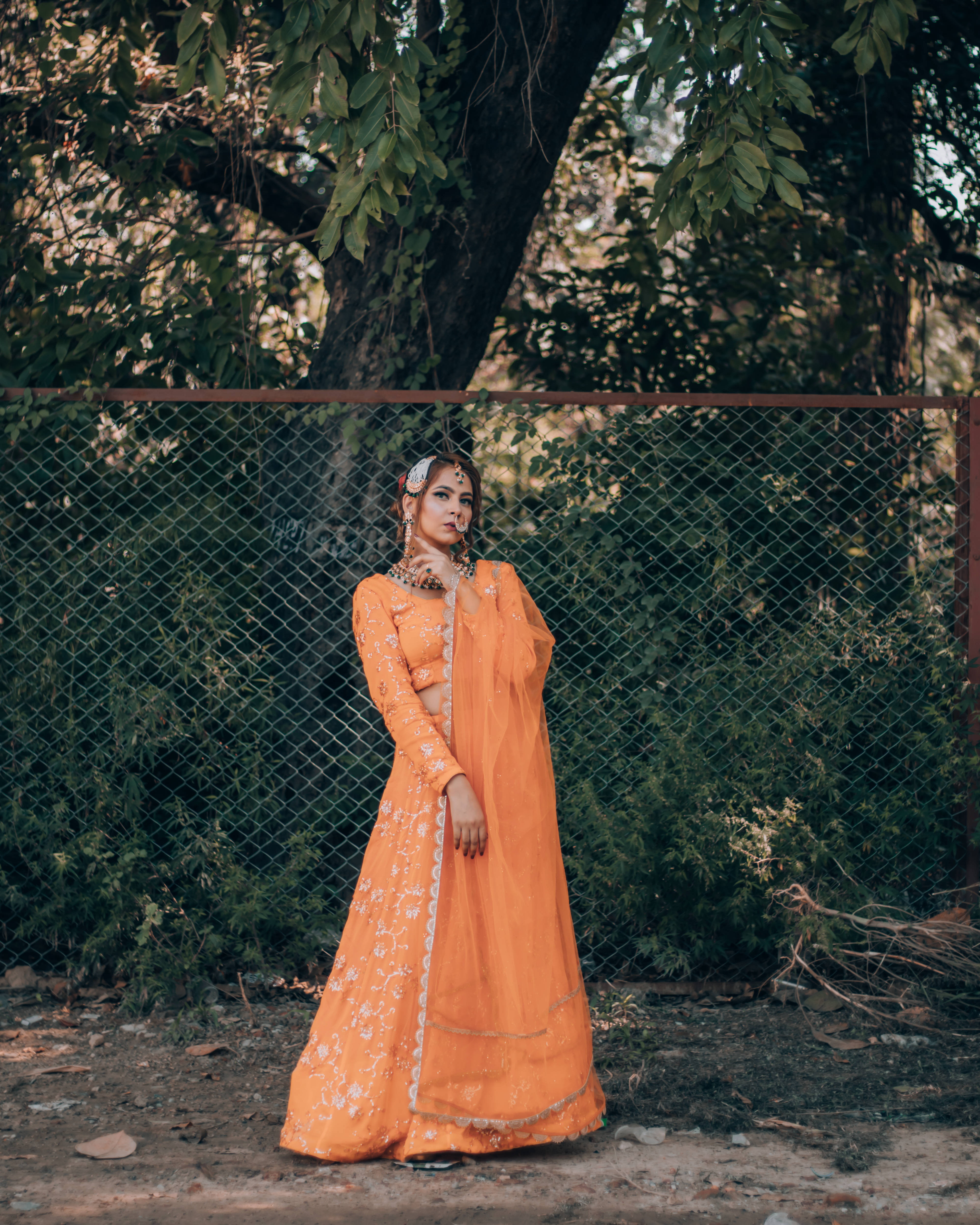 orange embroidered lehenga, chain-link fence, dappled sunlight, 4K Phone Wallpaper