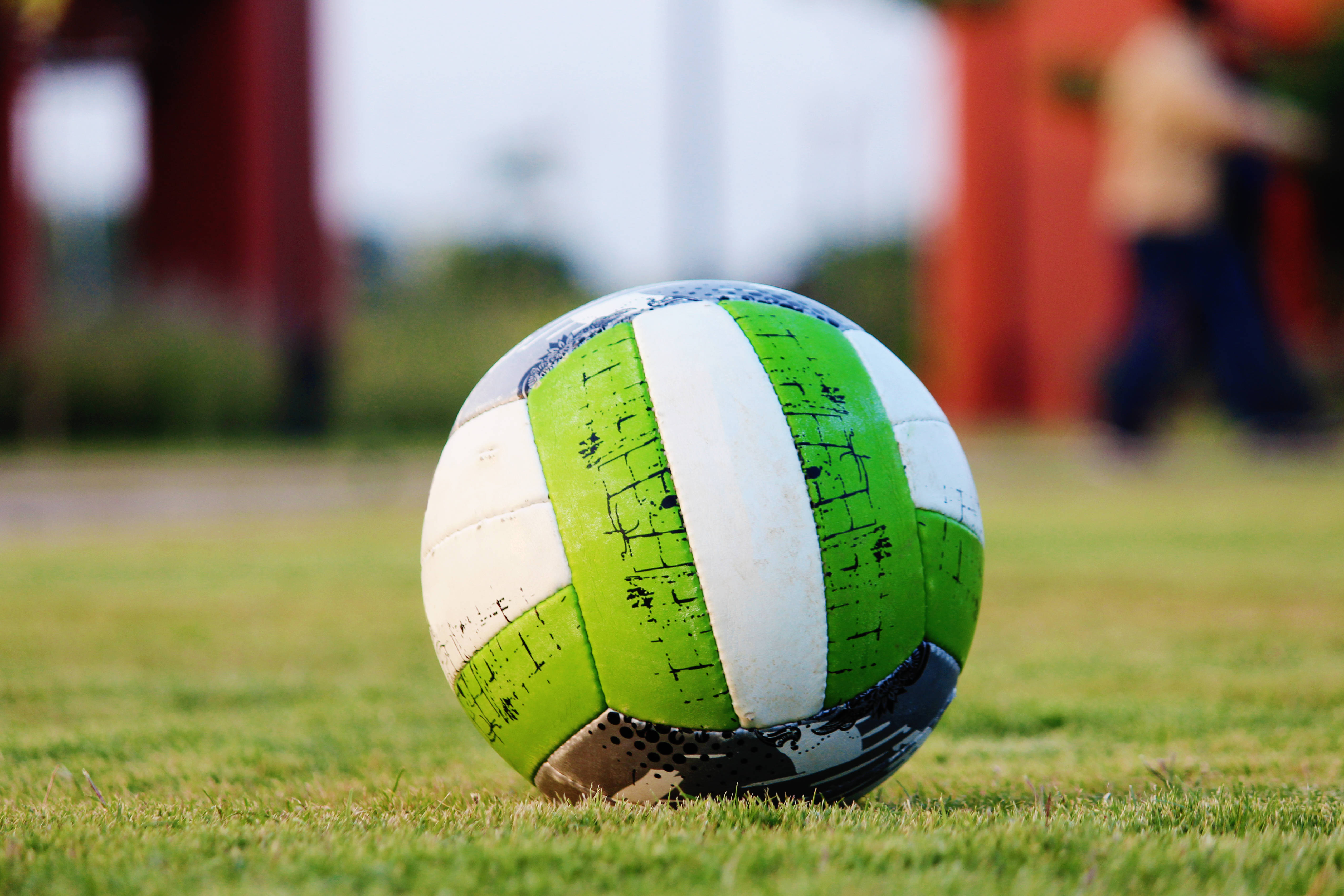 green and white soccer ball, vibrant grass, blurred red structures, 4K Desktop Wallpaper