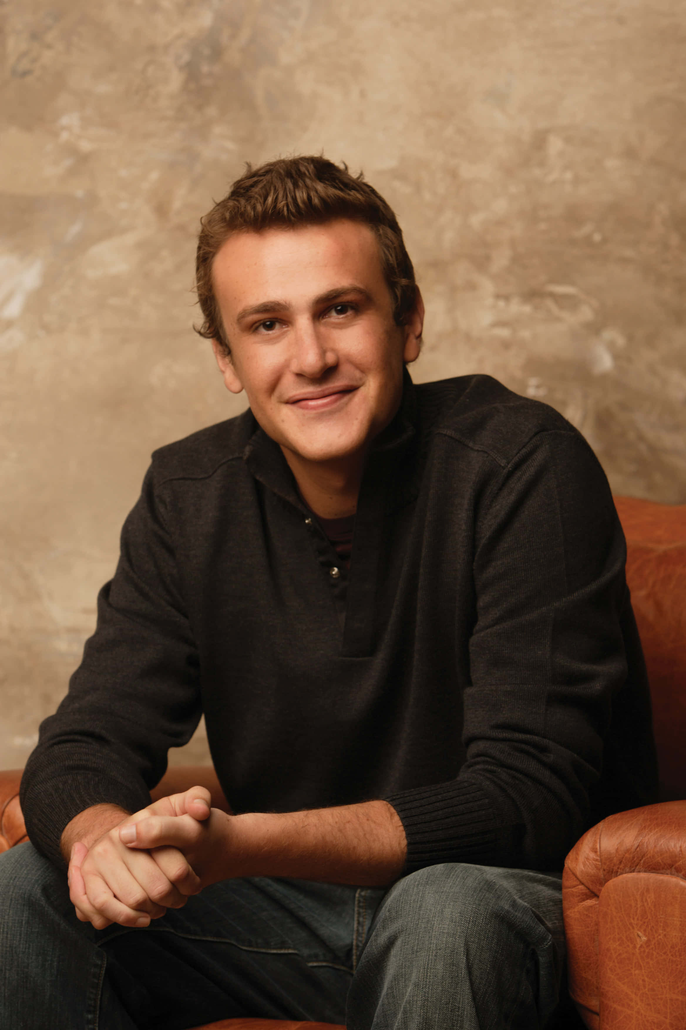 Jason Segel, brown leather armchair, textured beige wall, 2K Phone Wallpaper
