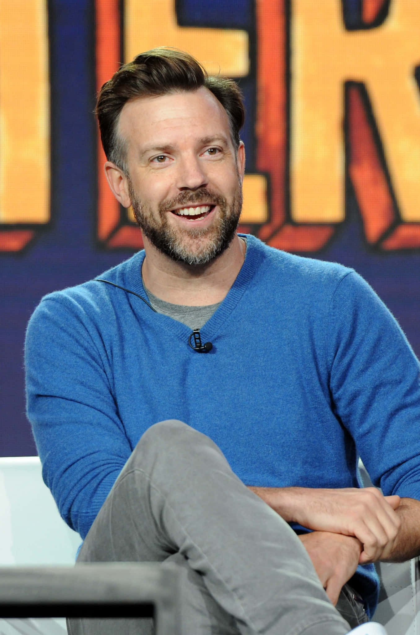 Jason Sudeikis, blue sweater, colorful superhero logo backdrop, Full HD Phone Wallpaper