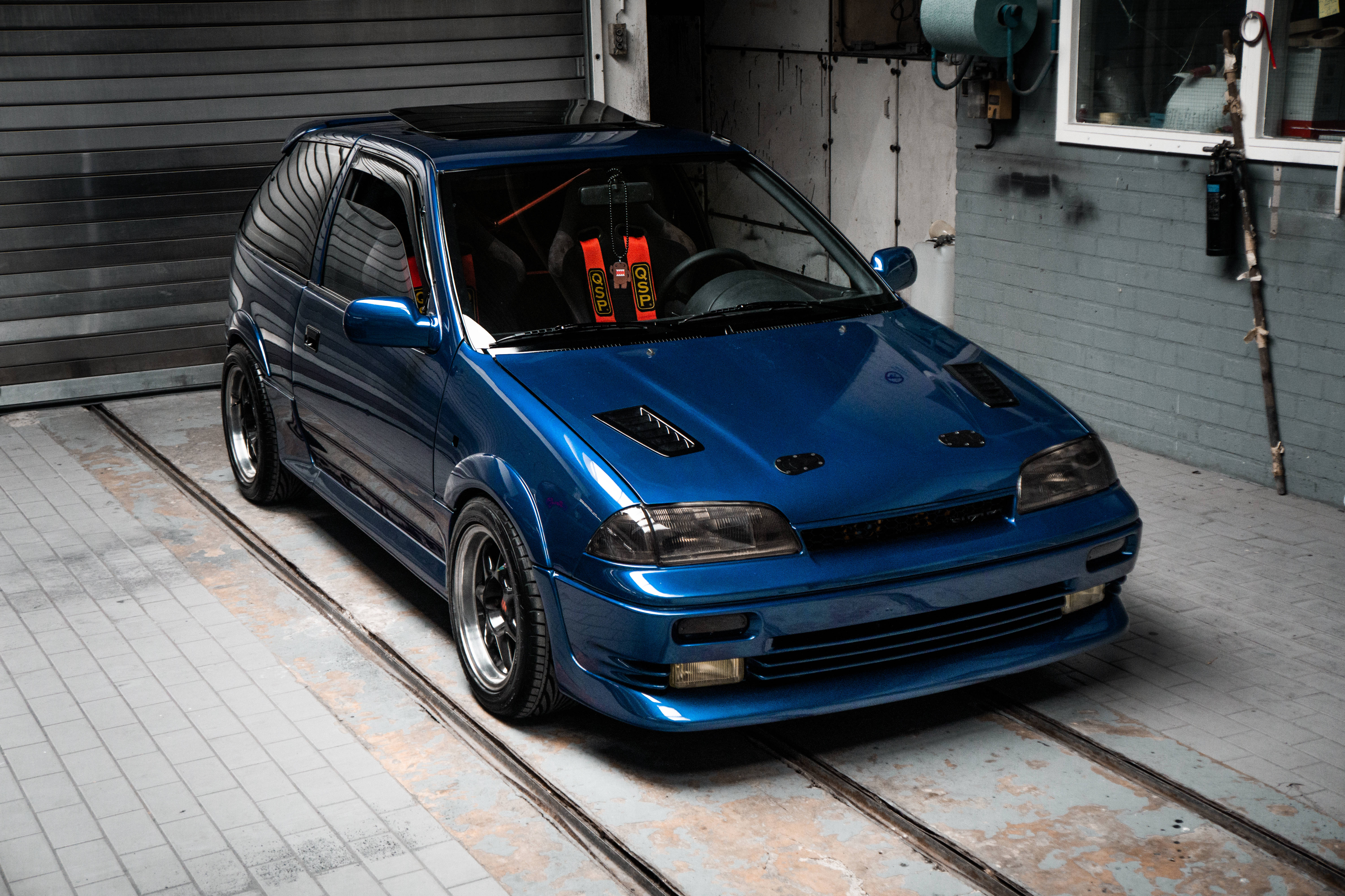 glossy blue modified hatchback, metal tracks, weathered garage, 5K Desktop Wallpaper