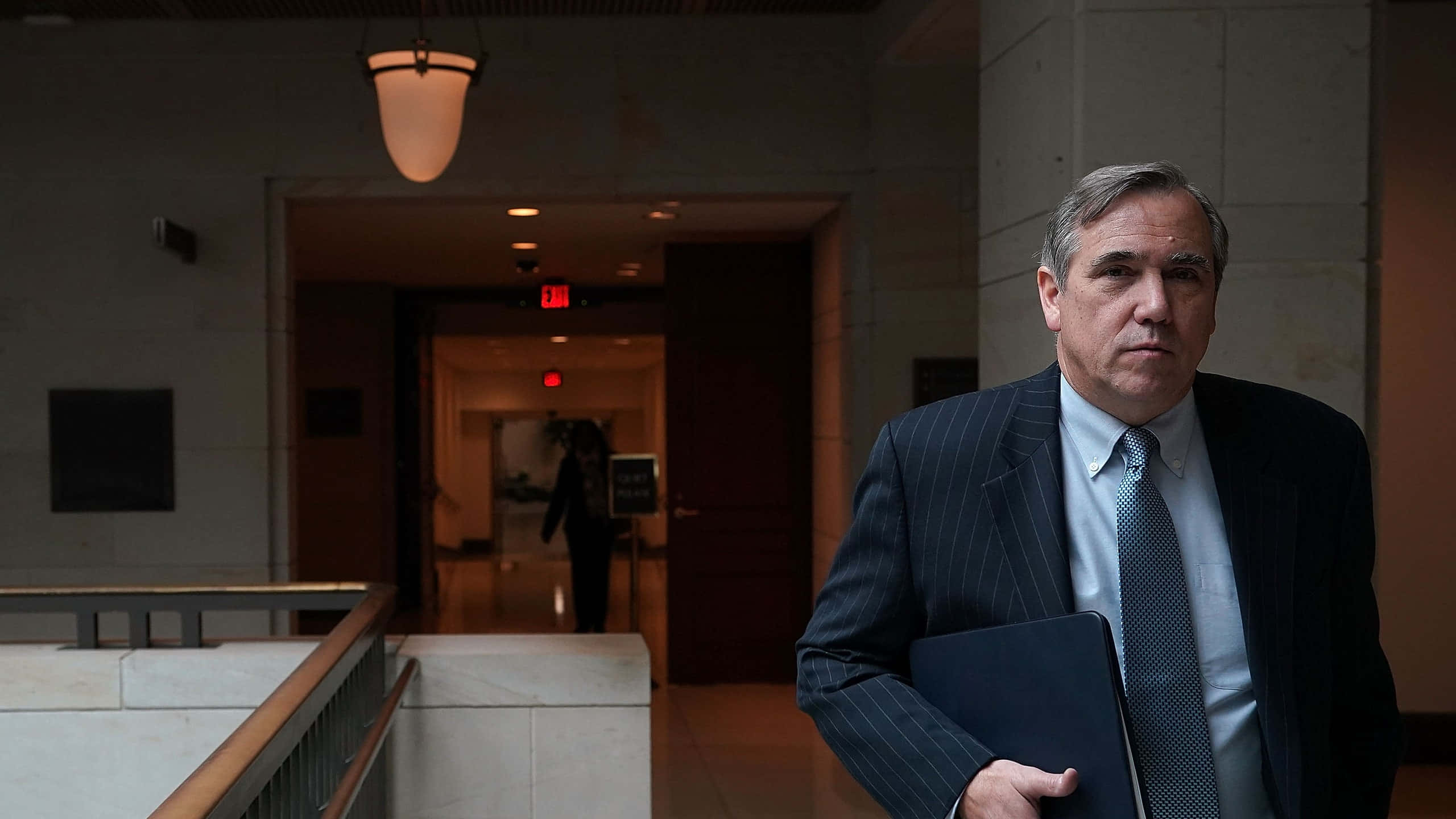 Jeff Merkley, pinstripe suit, dimly lit institutional hallway, 2K Desktop Wallpaper