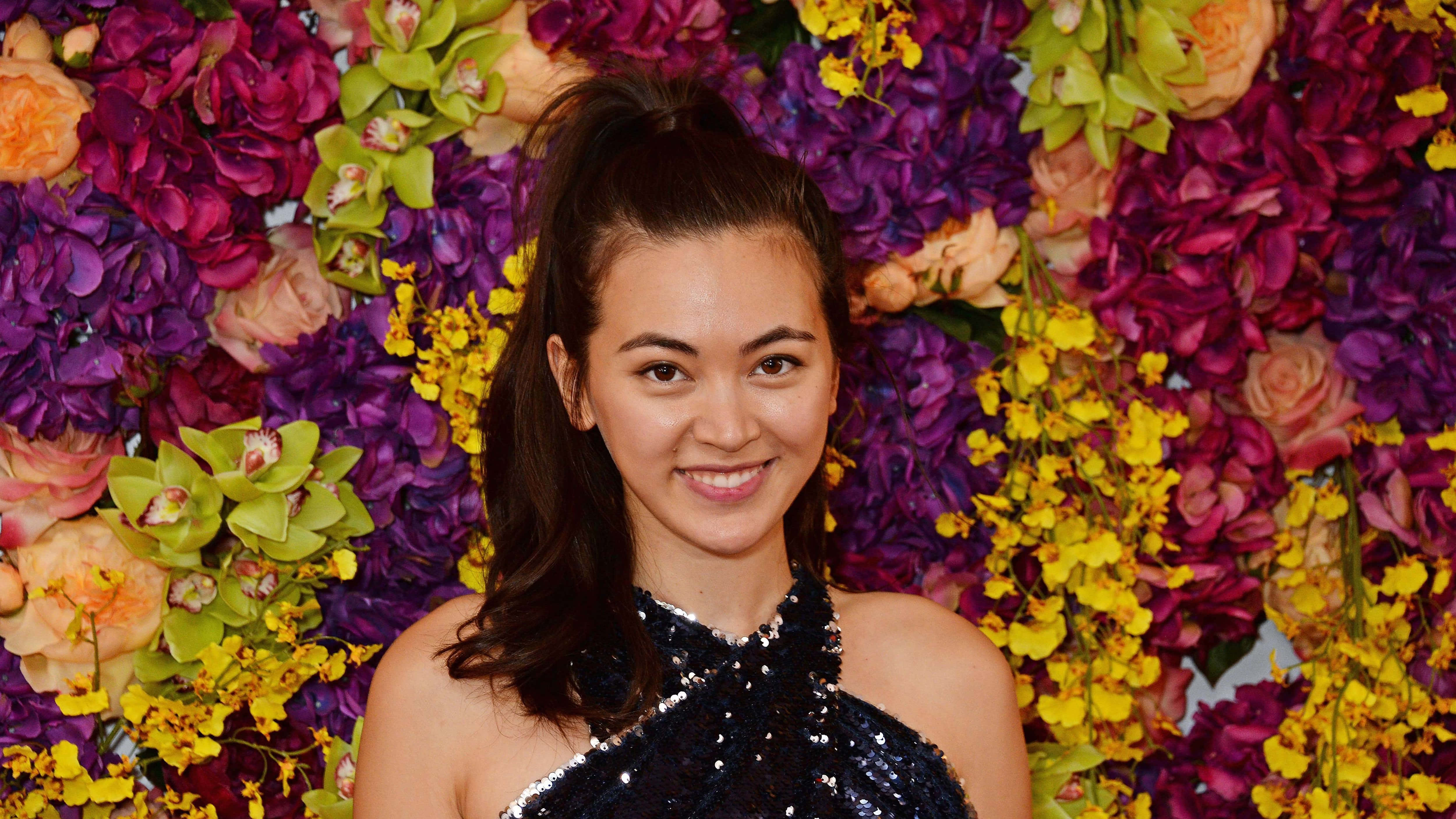 Jessica Henwick, sparkling black dress, vibrant wall of purple yellow and peach flowers, 4K Desktop Wallpaper