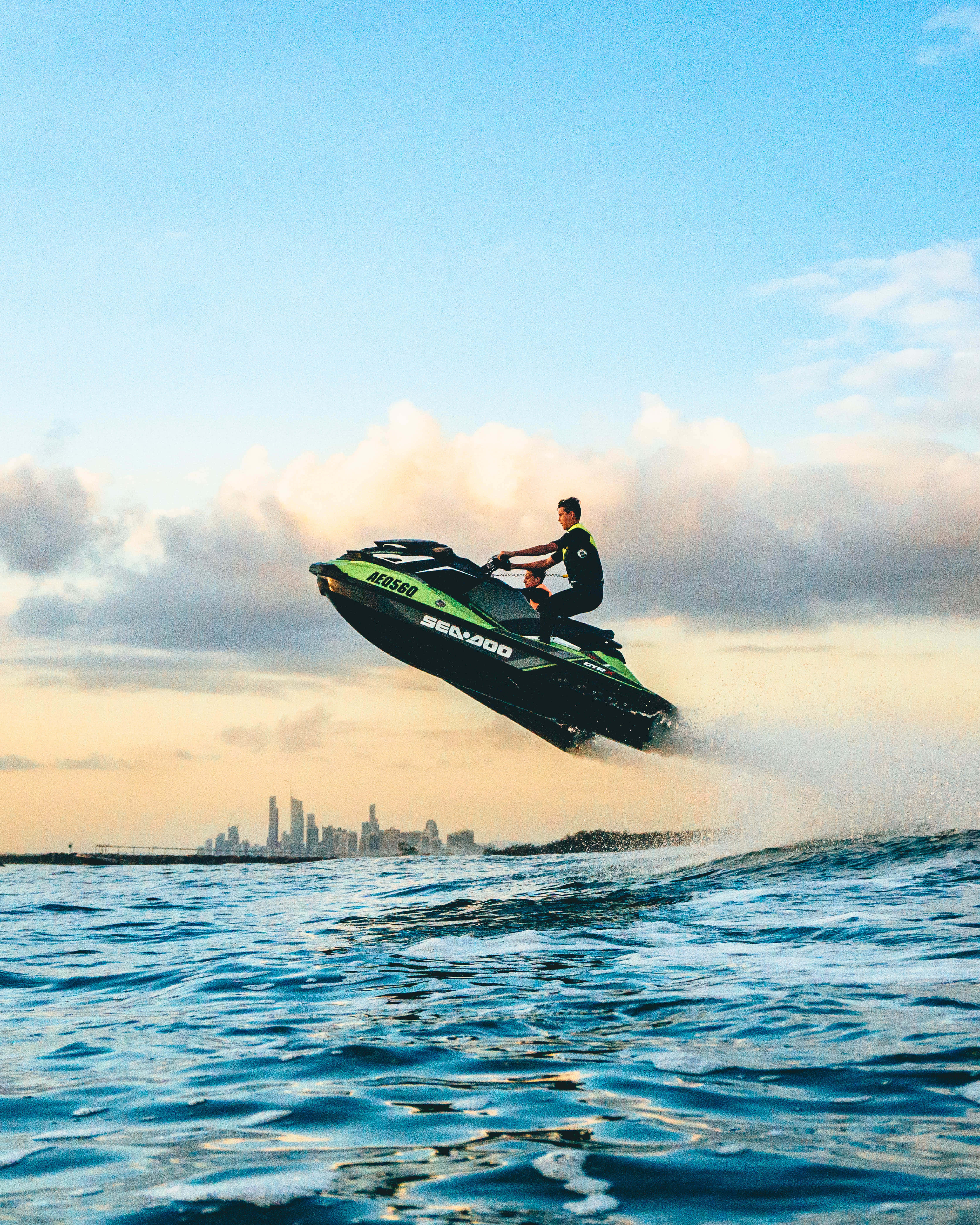green and black Sea-Doo jet ski, ocean waves, city skyline, 5K Phone Wallpaper