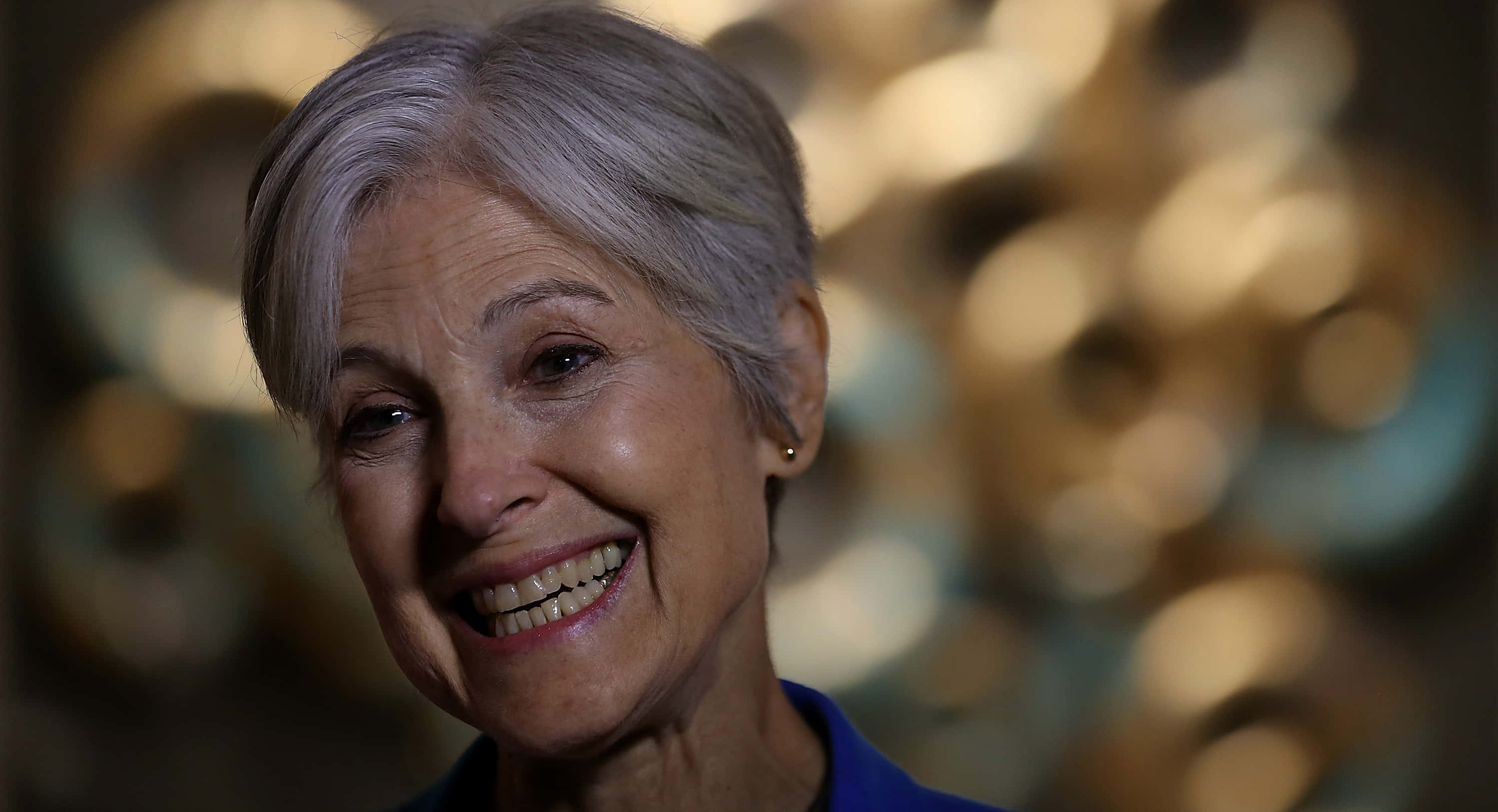 Jill Stein, gray hair, golden bokeh background, 2K Desktop Wallpaper