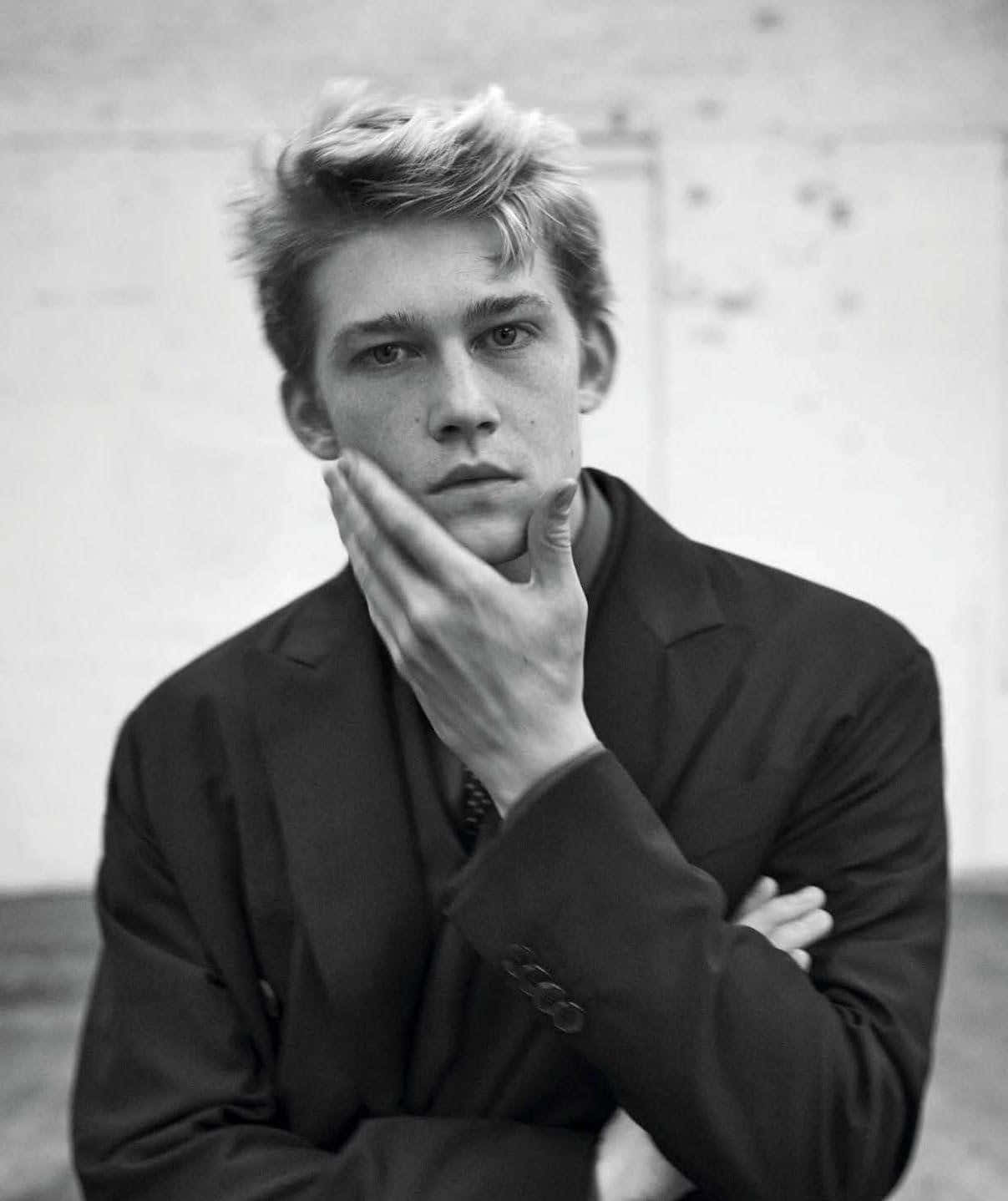 Joe Alwyn, dark suit, plain textured wall, HD Phone Wallpaper