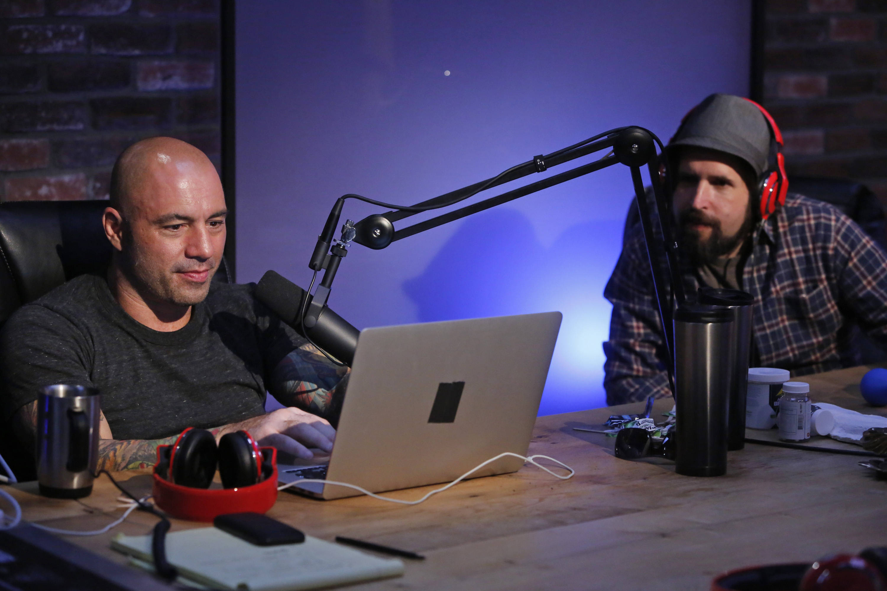 Joe Rogan, laptop, wooden desk, 2K Desktop Wallpaper