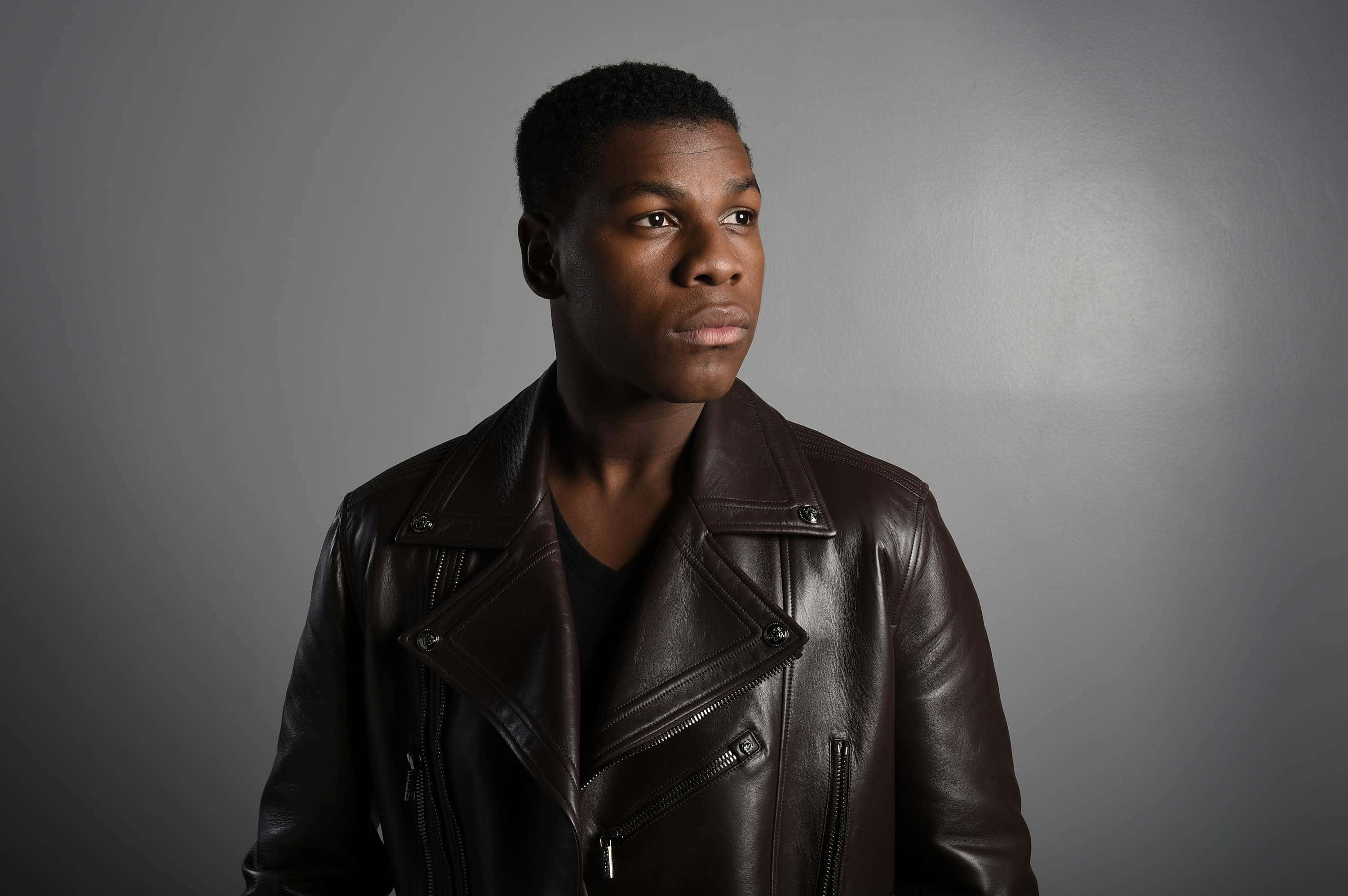 John Boyega, brown leather jacket, soft gray studio backdrop, 2K Desktop Wallpaper