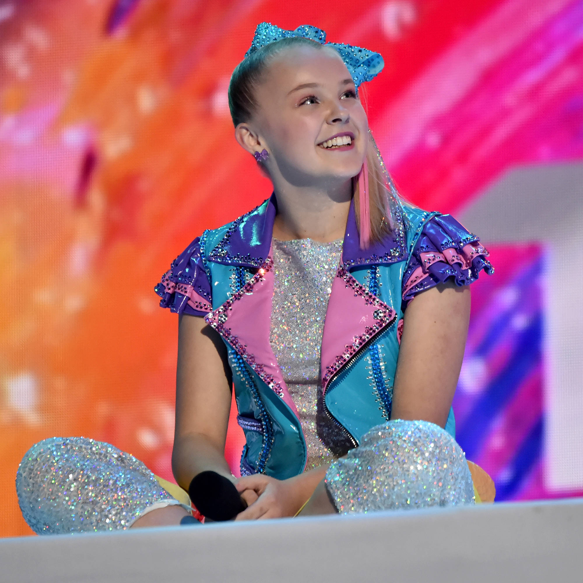 Jojo Siwa, glittering blue pink and silver outfit, sitting on stage, Full HD Desktop Wallpaper