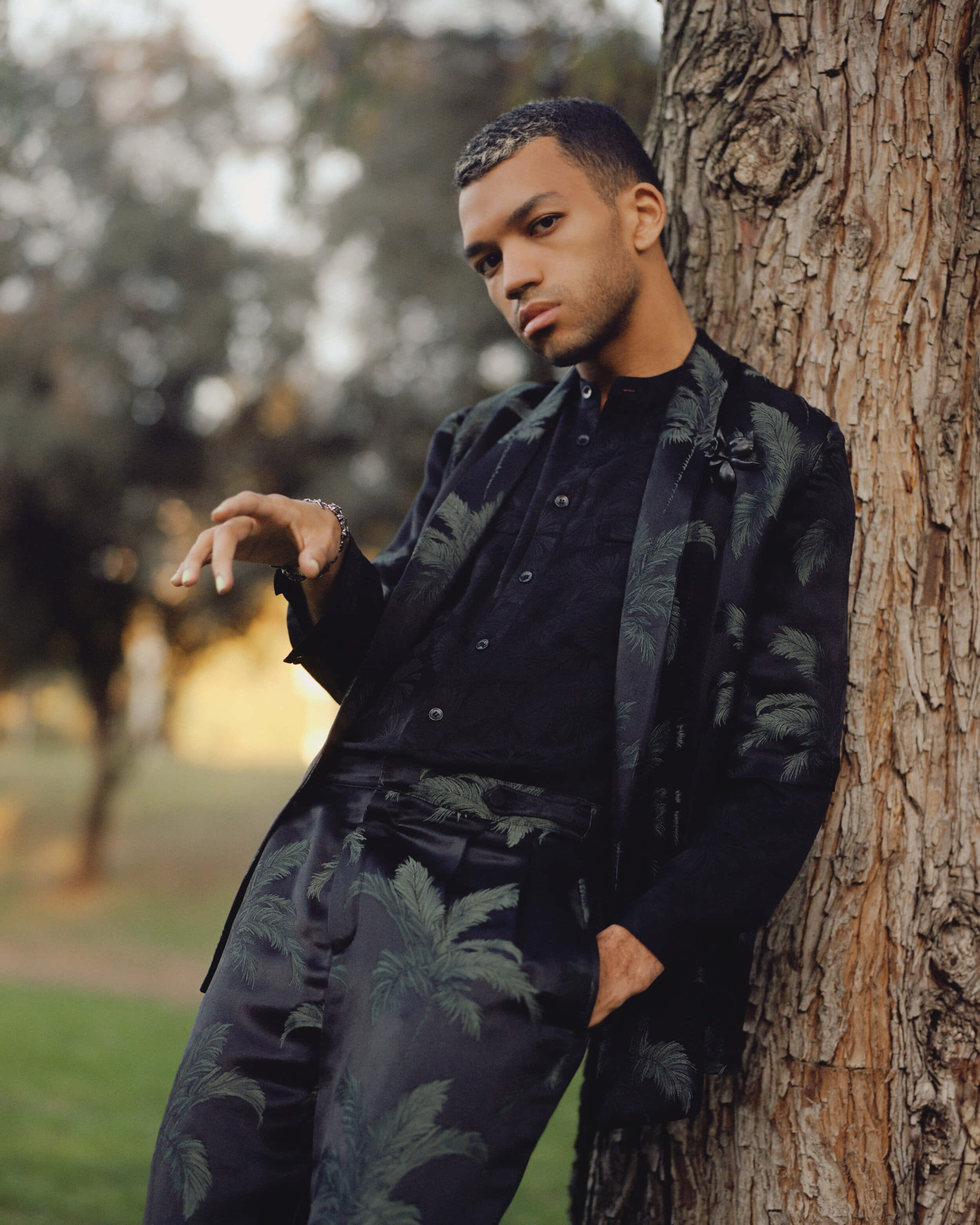 Justice Smith, palm-printed attire, textured tree trunk, 2K Phone Wallpaper