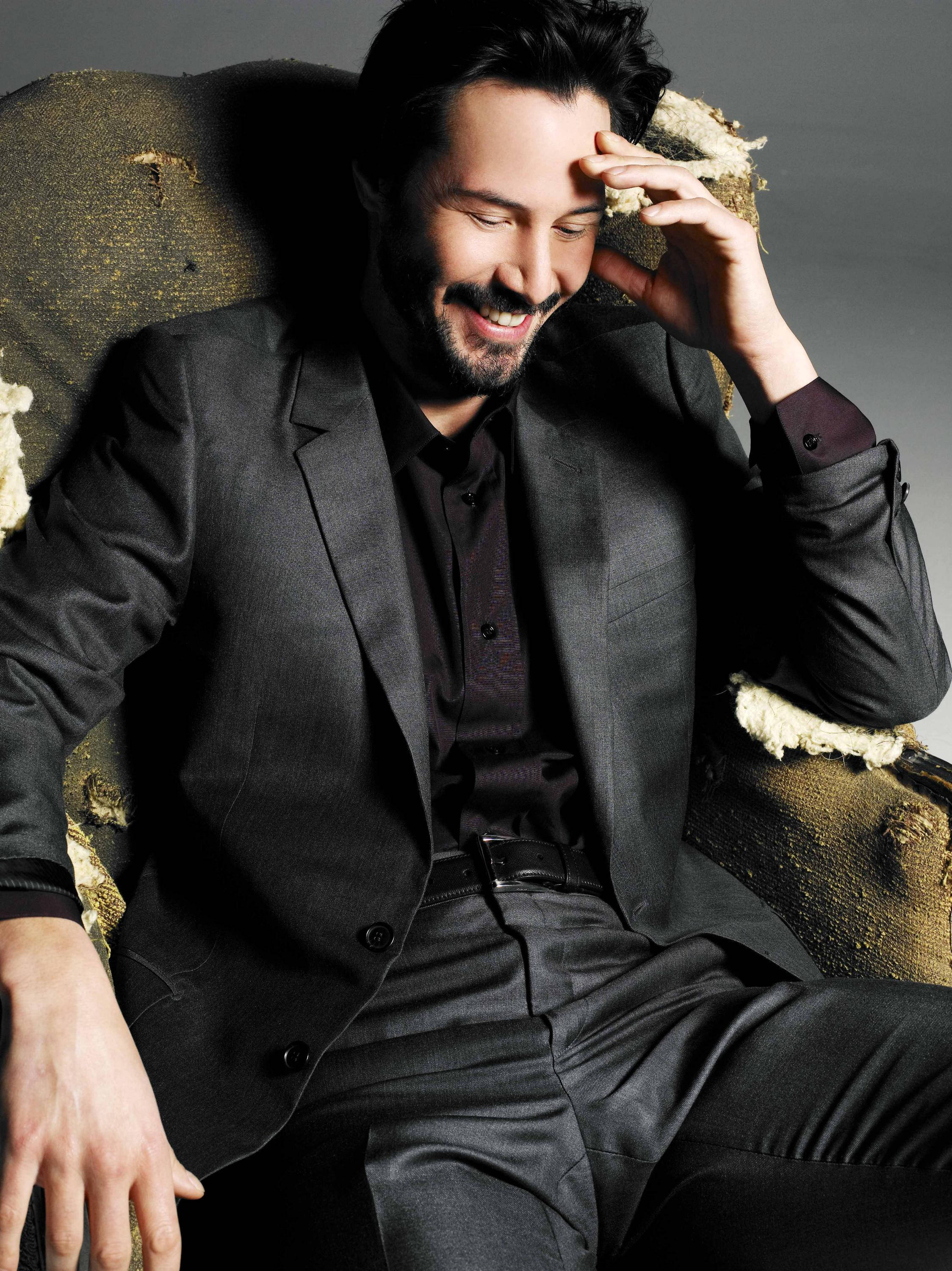 Keanu Reeves, dark suit, worn textured armchair, 2K Phone Wallpaper